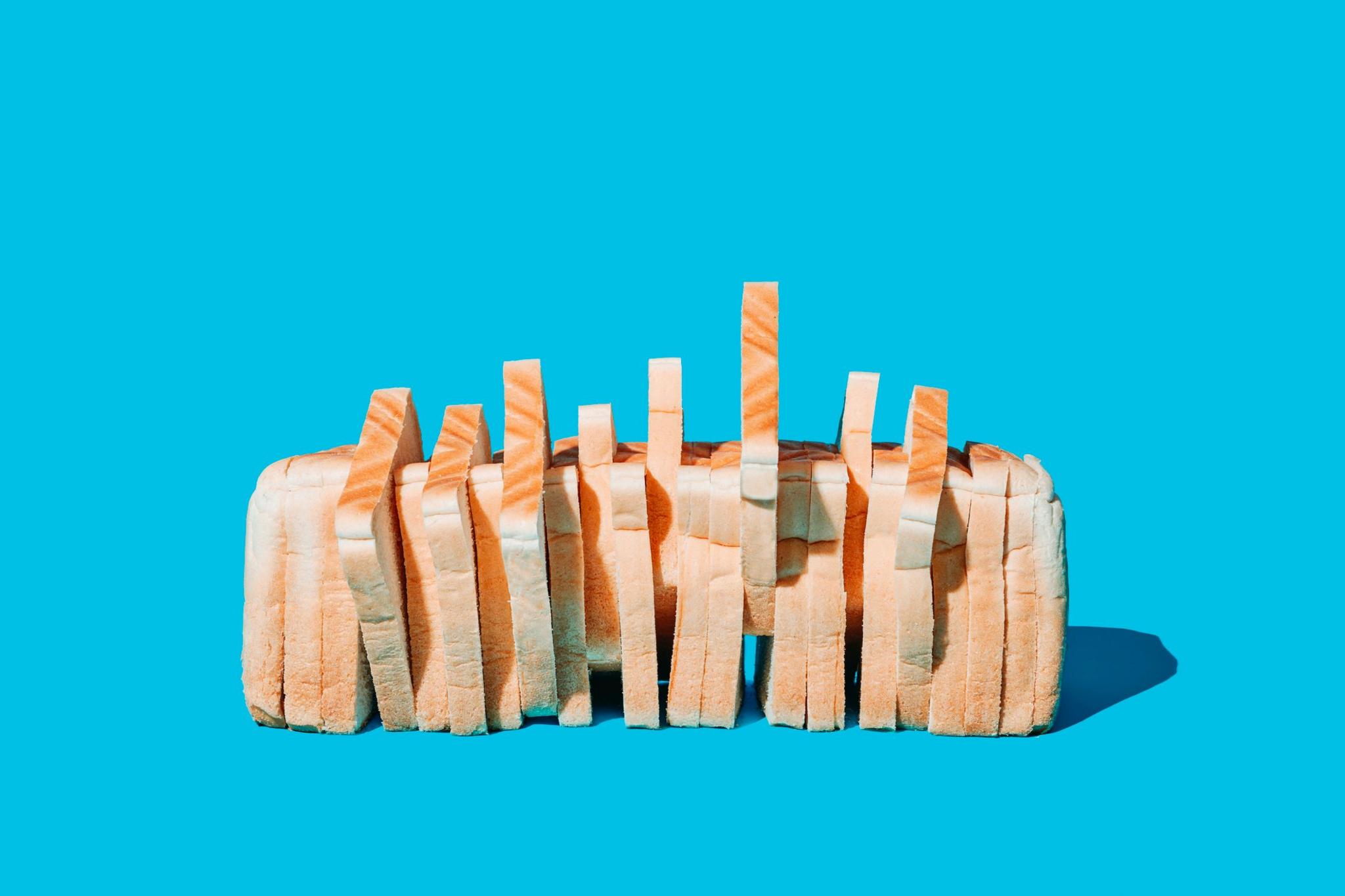 A loaf of white sliced bread with no packaging and some slices sticking up a little. On a bright blue background