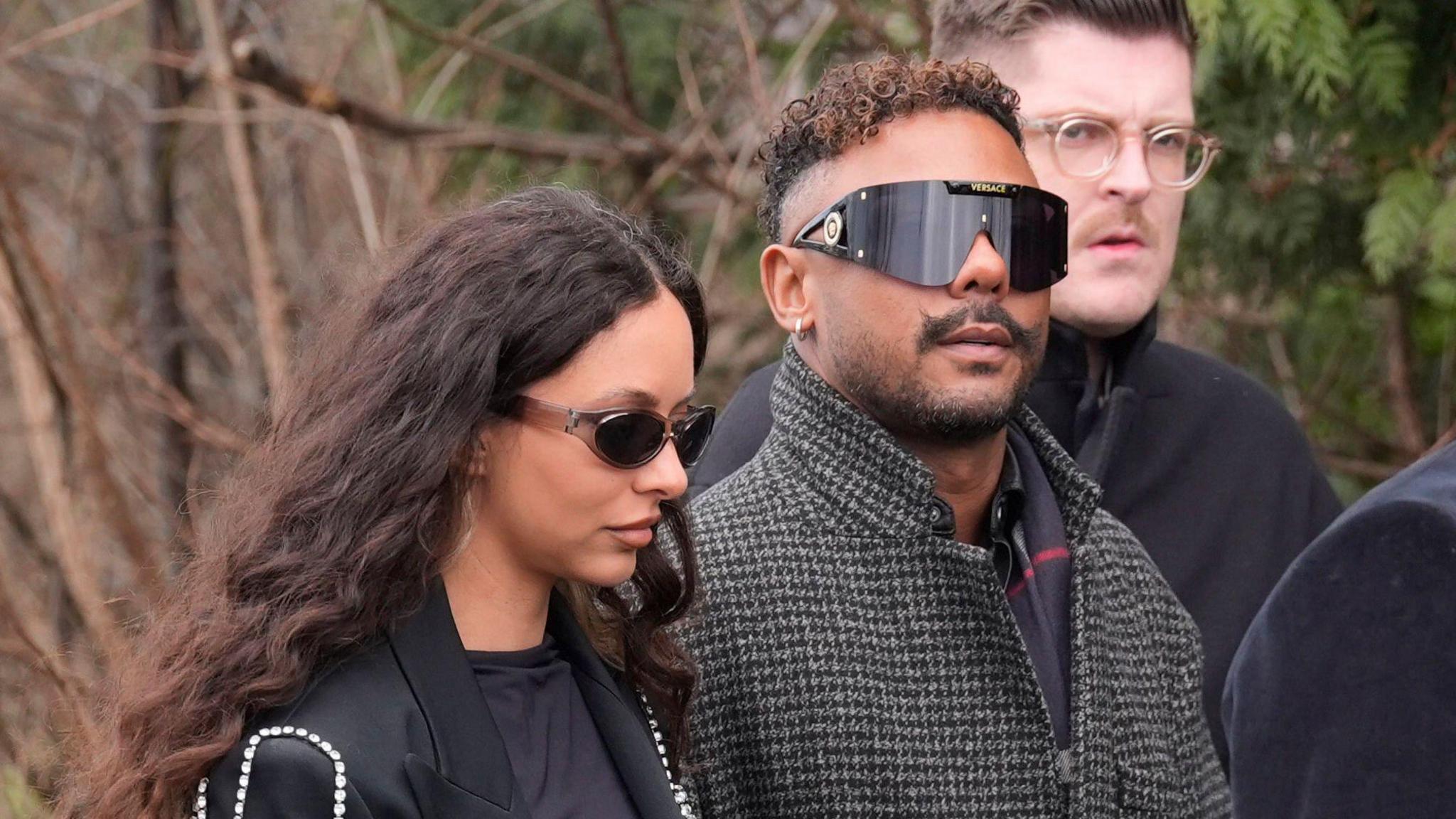 In a close-up shot, Jade Thirlwall and Marcus Collins are pictured walking towards the church for the ceremony. Jade looks straight ahead of her, wearing a dark blazer, while Marcus is looking up towards the camera. Both are wearing sunglasses.