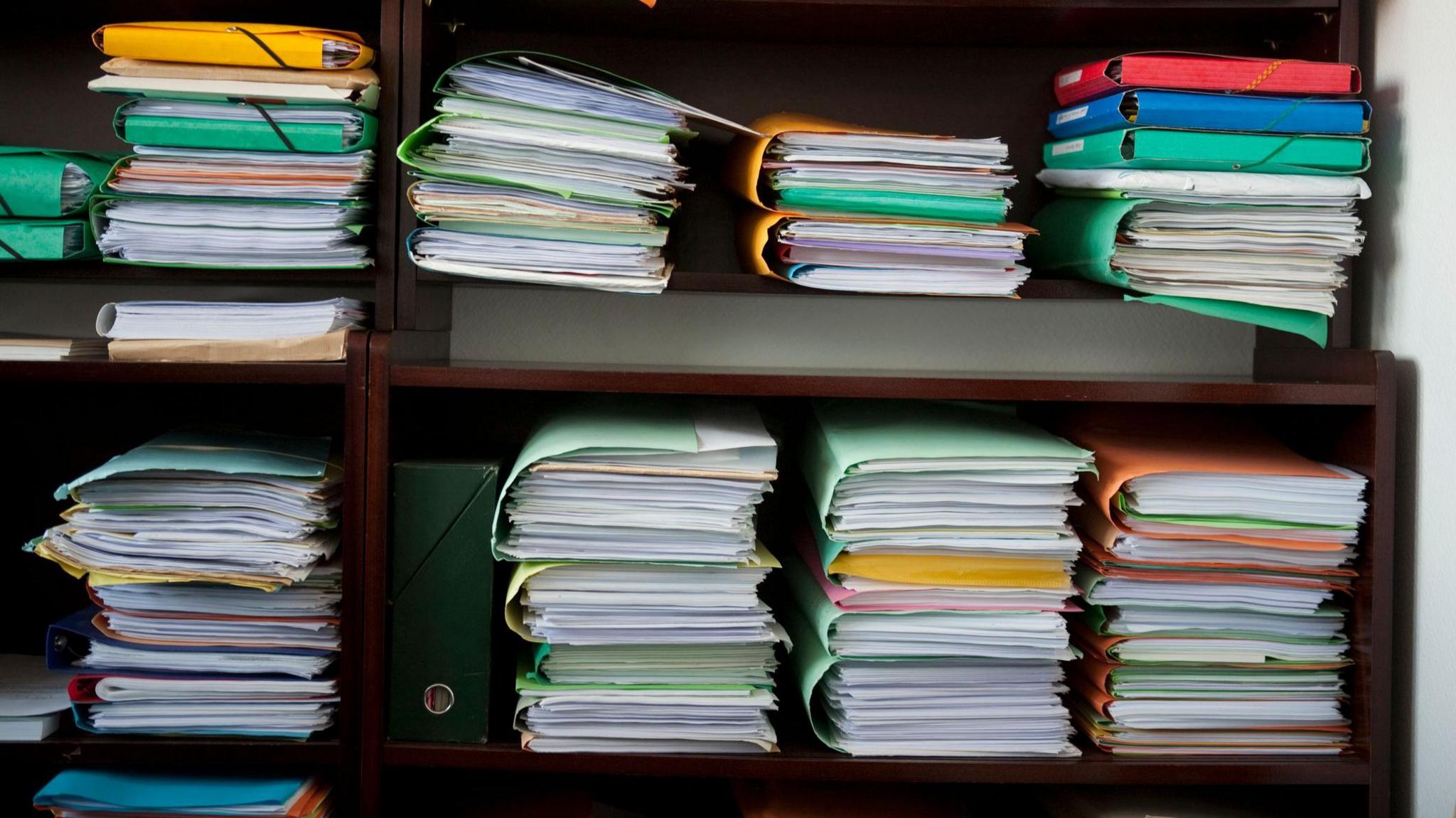 Multiple folders in a bookcase with many pieces of paper in each one. 