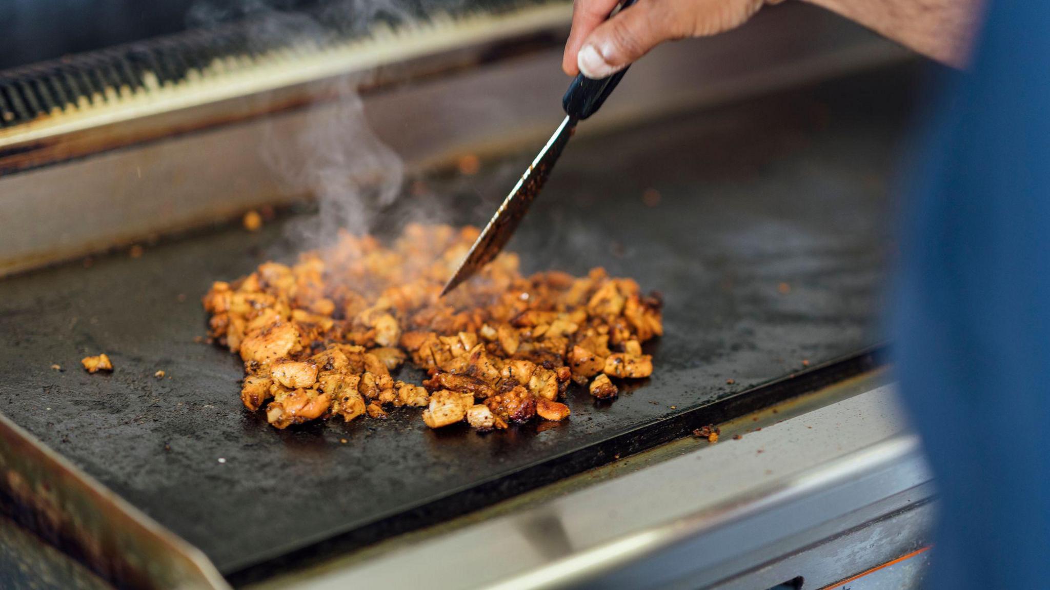 A general image of a man preparing food in the kitchen, frying chicken on a grill.
