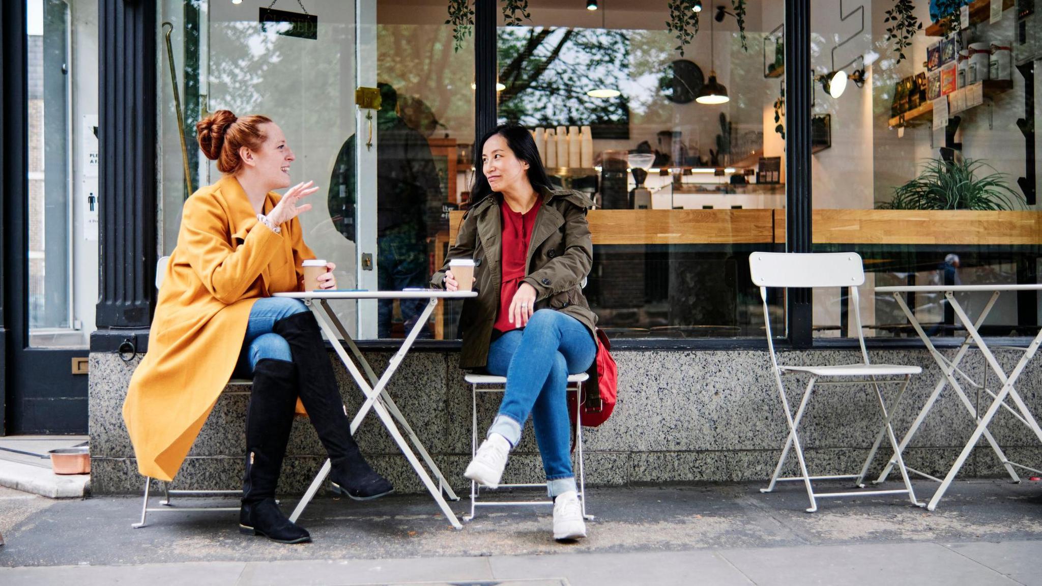 Woman gesturing while talking with female friend outside coffee shop