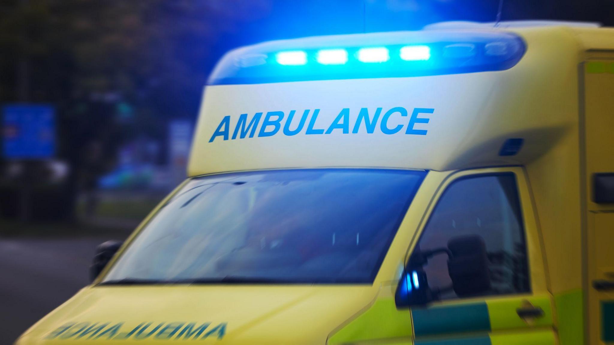 A close-up image of the front of a yellow ambulance with its blue lights on.