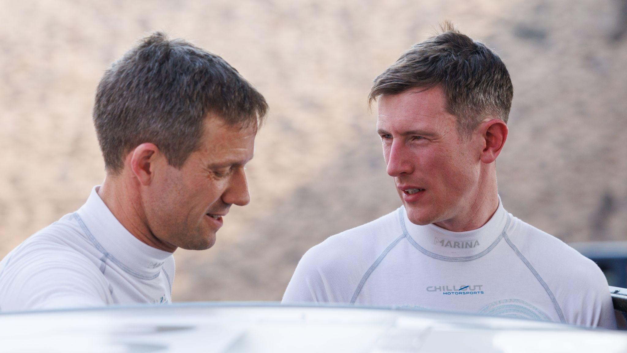 Sebastien Ogier and Elfyn Evans talk adjacent to a car