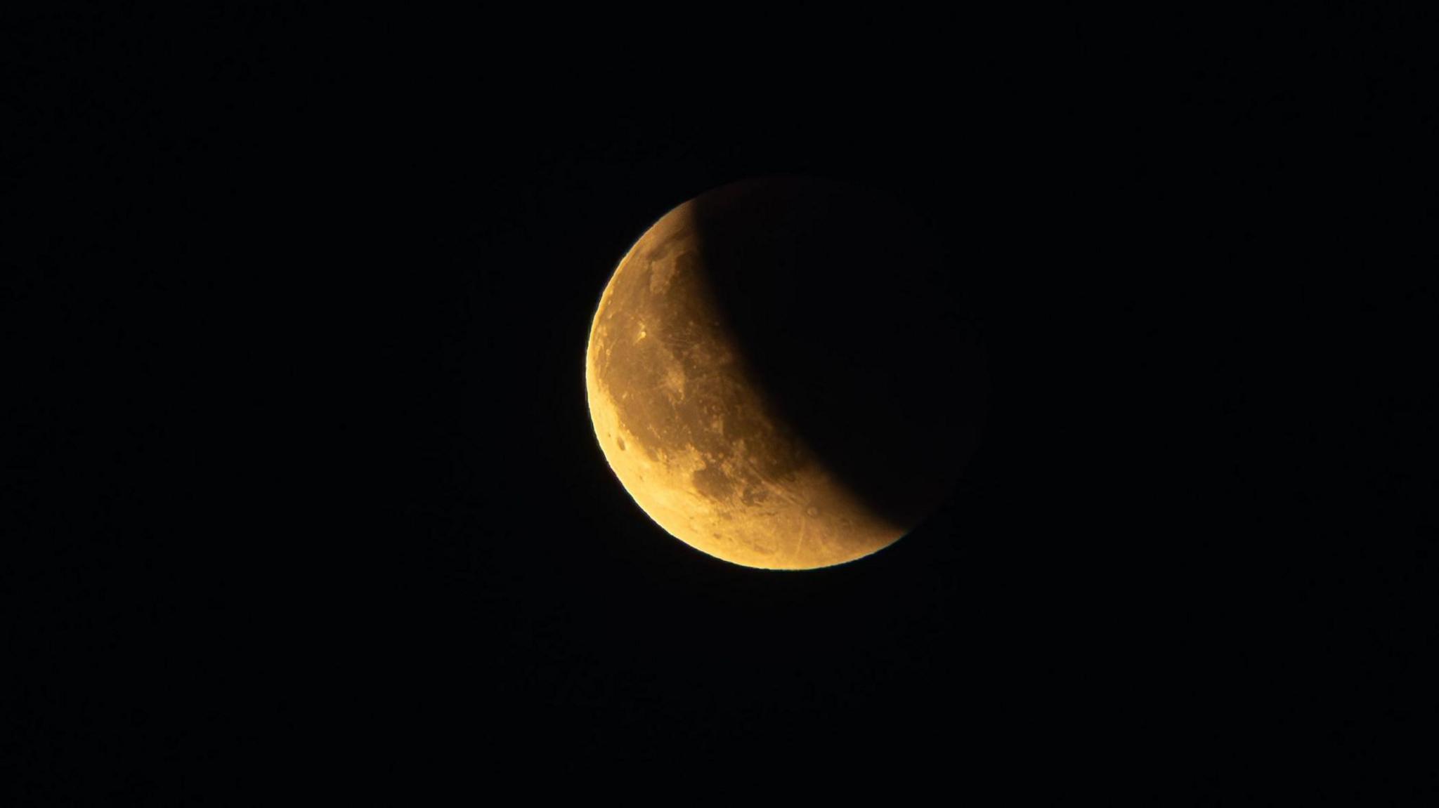 A yellowy moon partially obscured due to the eclipse. The moon is taken against a black background. 