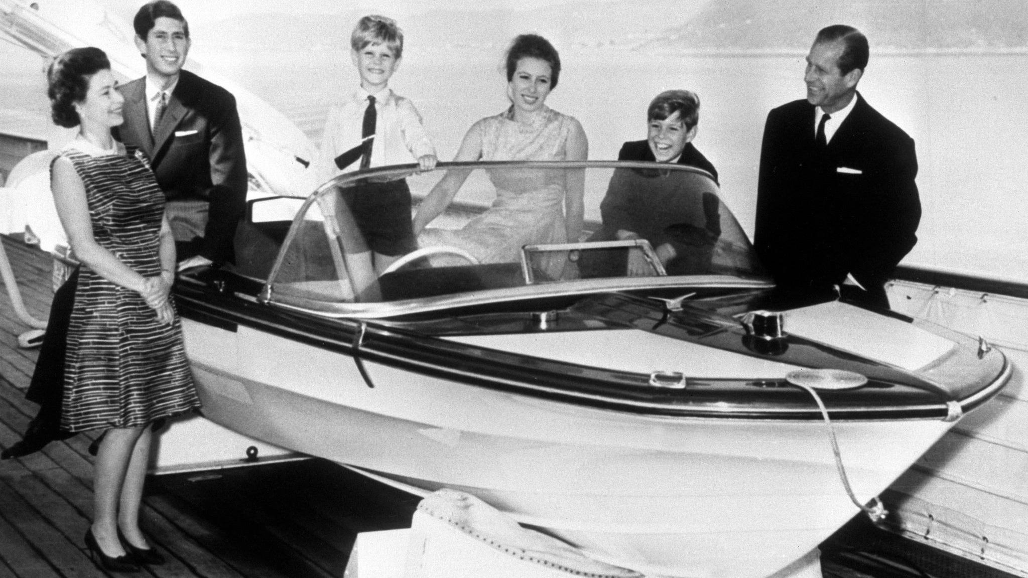 The royal family's 1969 card features a black-and-white photograph of them gathered around a speed boat on land. All are smartly and formally dressed and smiling. The Queen, the Duke of Edinburgh and Prince Edward are standing. Prince Charles, Princess Anne and Prince Andrew are sitting.