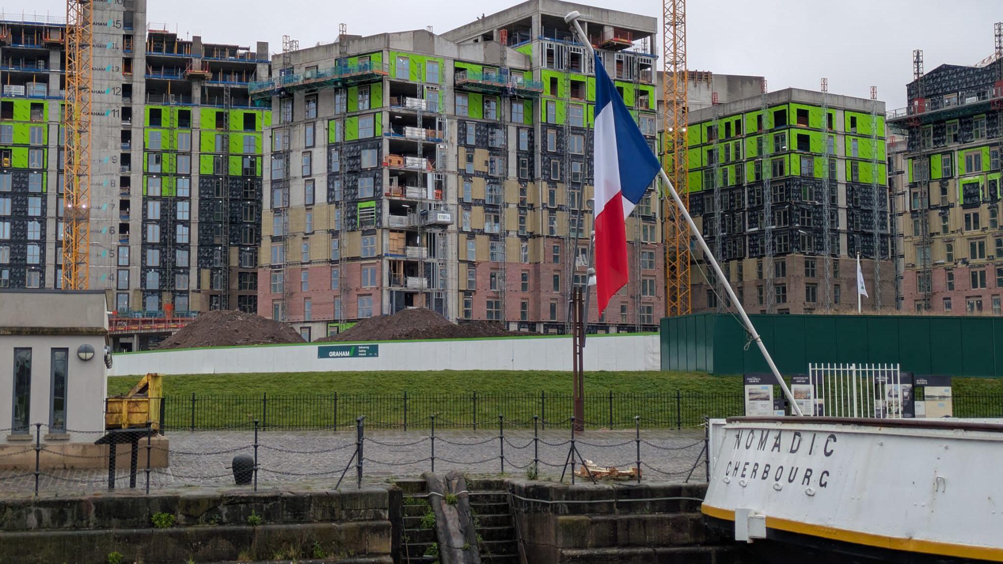 An apartment block covered in scaffolding and building materials. It is situated beside the SS Nomadic boat at the Titanic slipway.