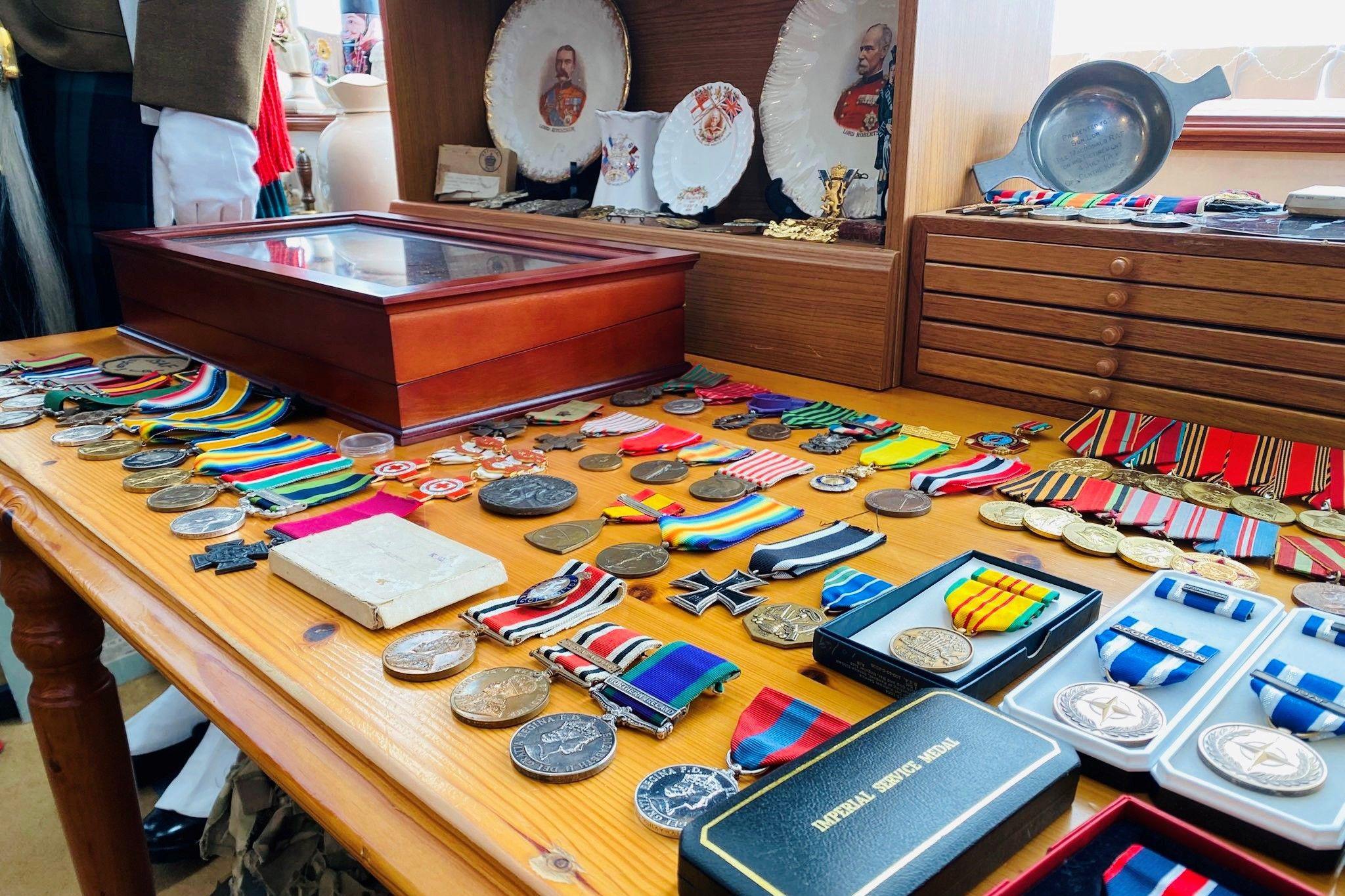 A large collection of medals on a table, with antique plates in the background on a shelf