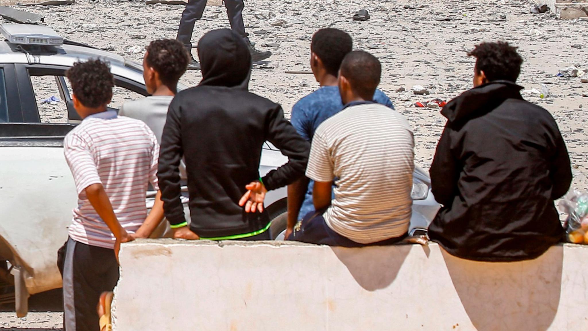 Young, male migrants sit outside a detention centre in Tripoli