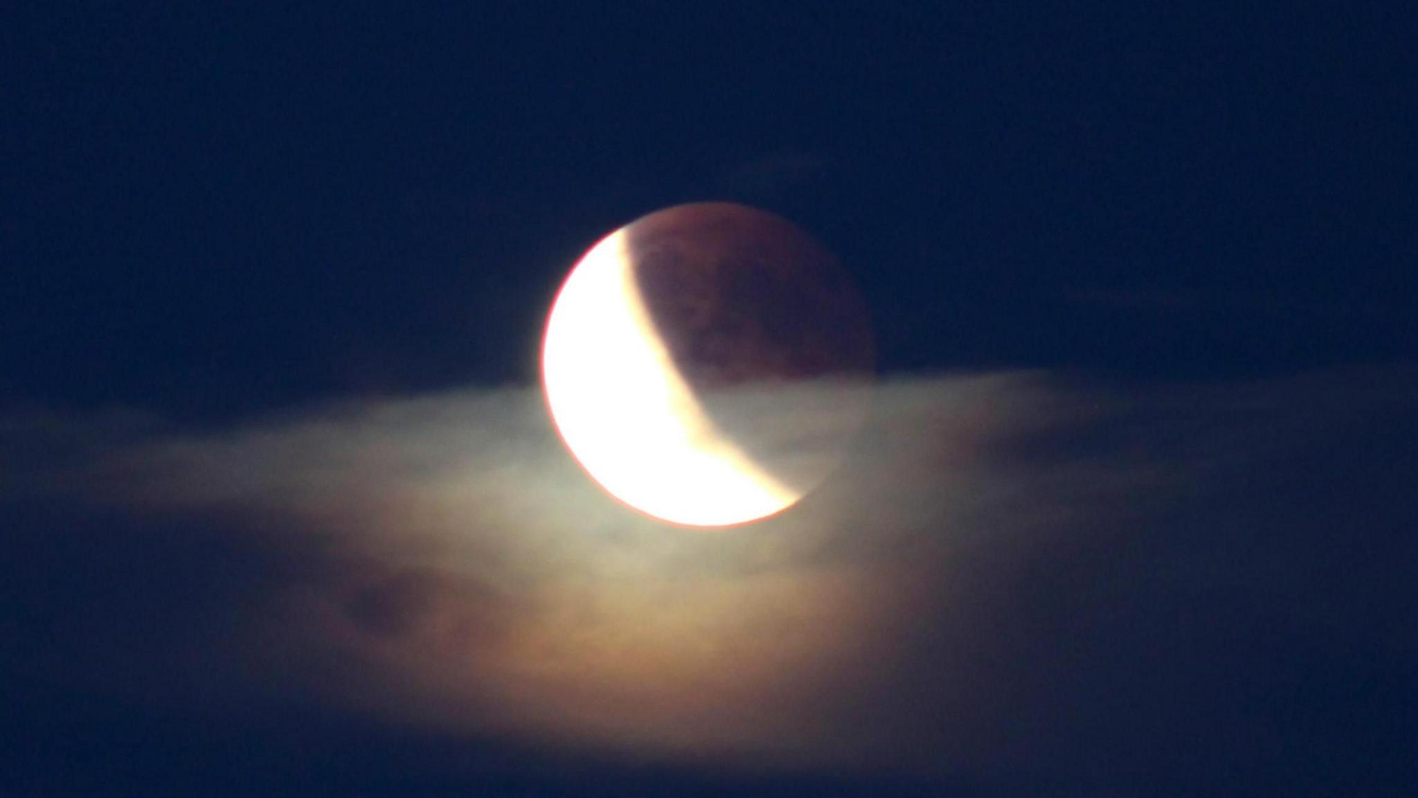 A full moon partially covered by a lareg illuminated section with a red tint.