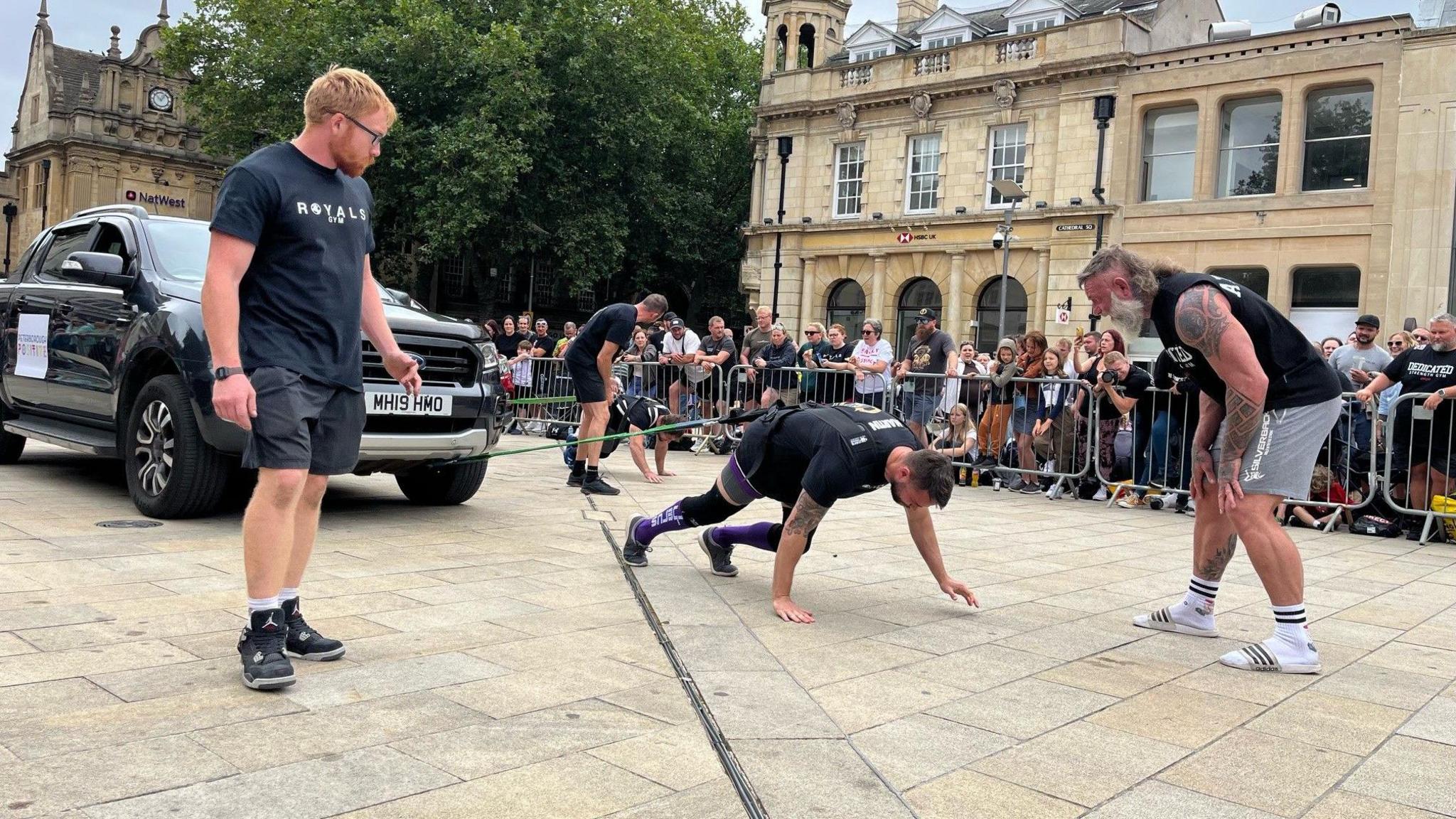 Man pulling a car with ropes while spectators watch