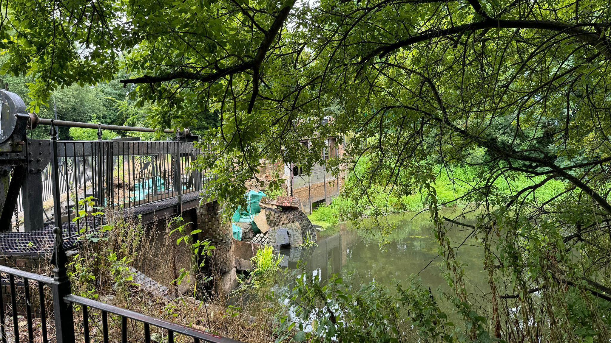 Brickwork from the Middle Mill weir that has collapsed into the River Colne, with foliage surrounding the river. 