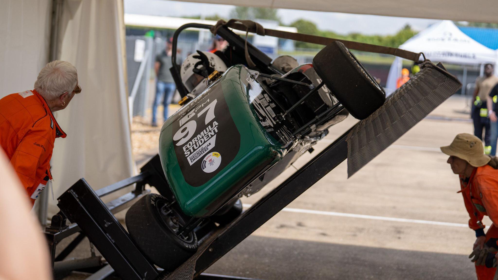 Green racing car tipped on its side with people looking underneath