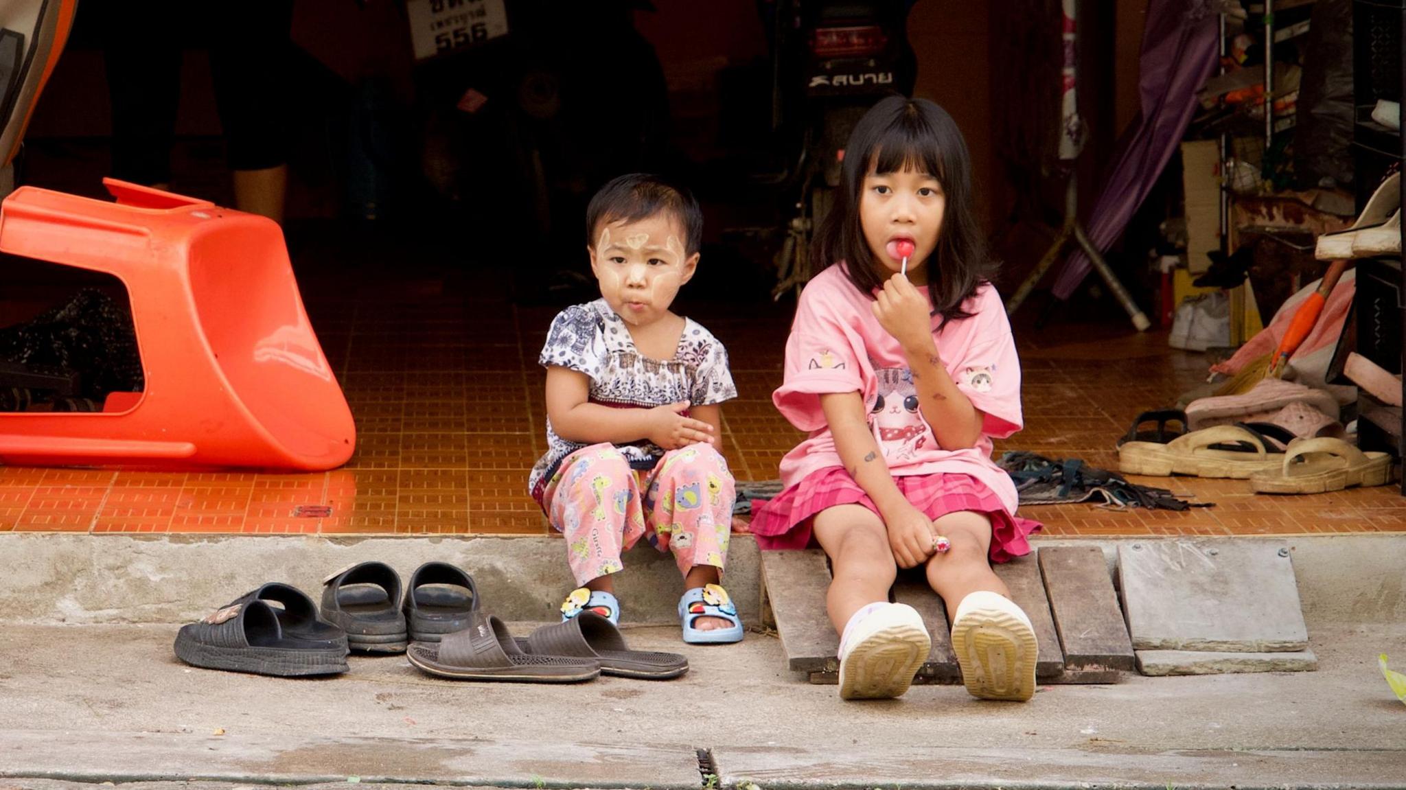 A young girl sitting on the roadside with another young child in Mae Sot, Thailand, on the border with Myanmar