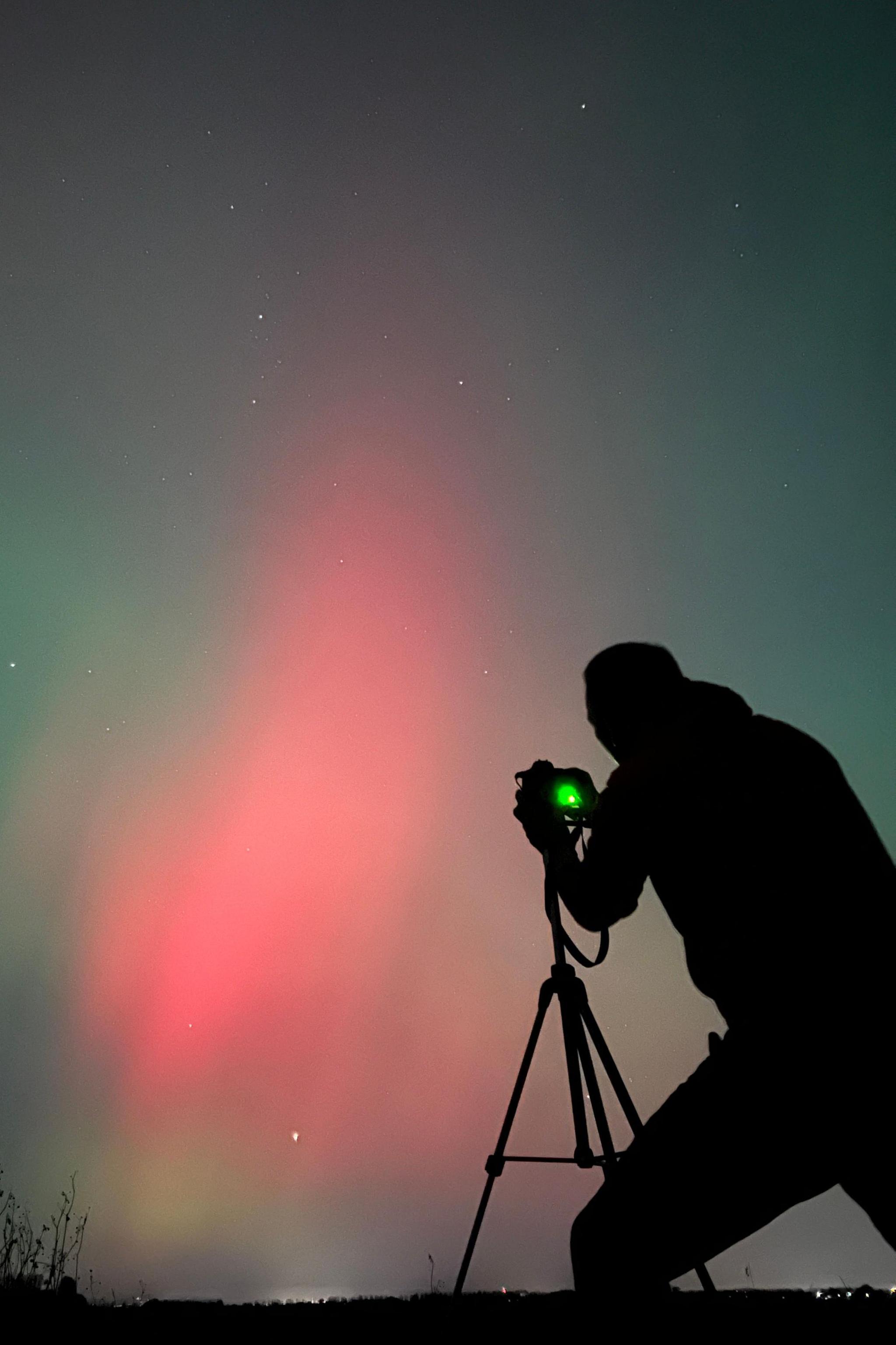 A man is silhouetted taking a picture of the pink and blue Northern Lights