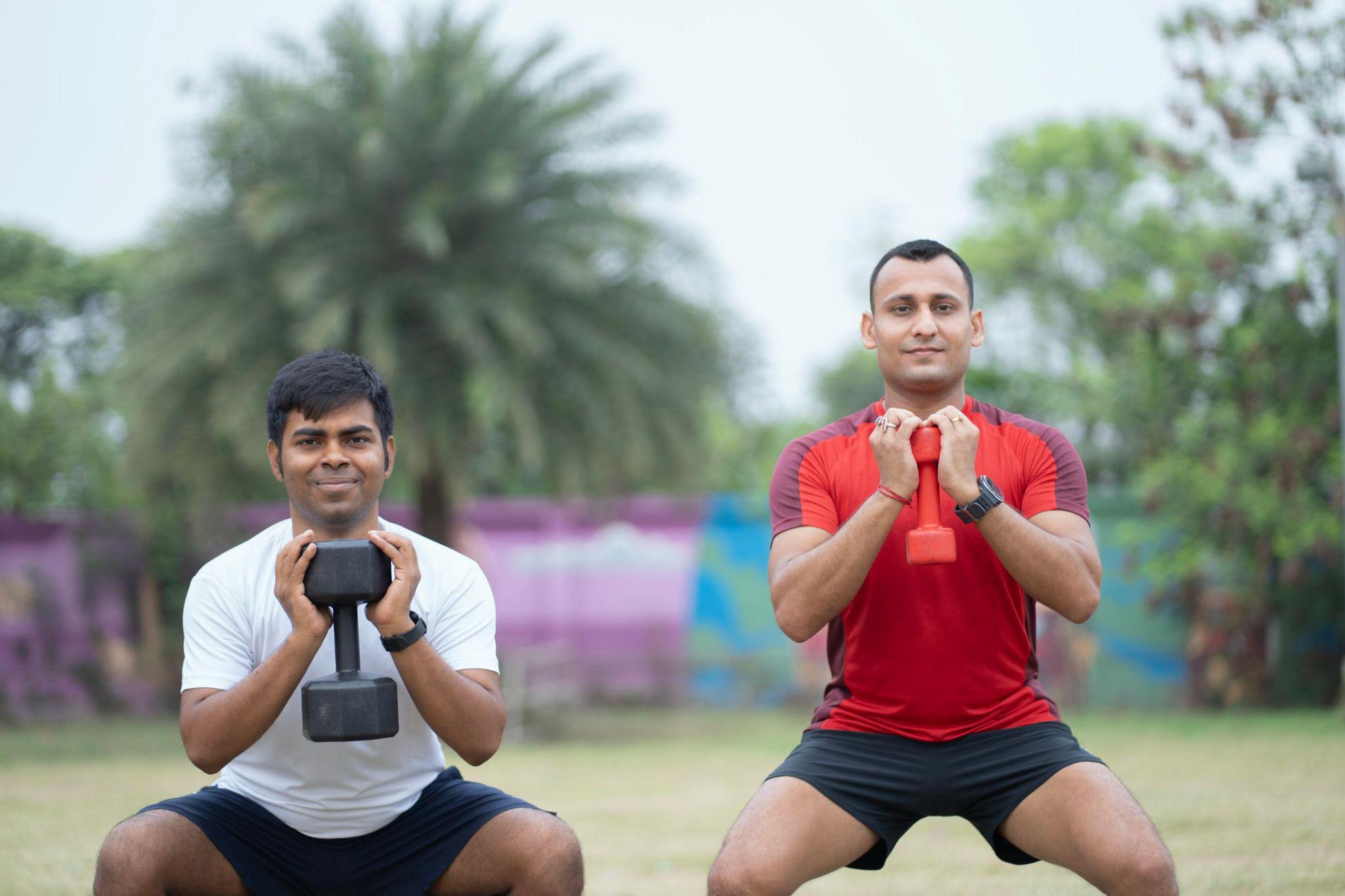Two men performing squats with dumbbells in an open outdoor environment. The image captures a moment of focused strength training, emphasizing dedication, fitness, and healthy lifestyle habits