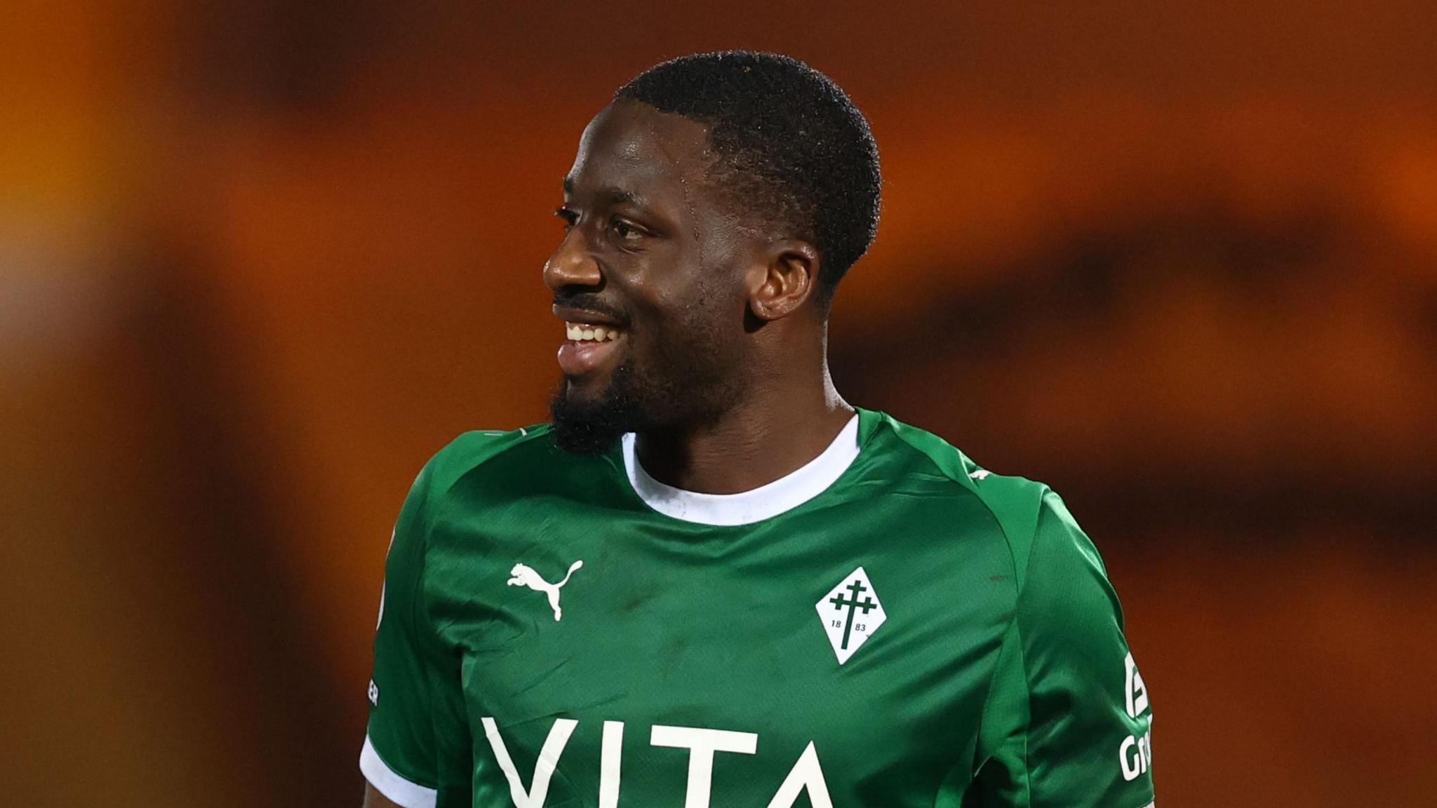 Joseph Olowu head and torso shot, smiling and looking to his right, wearing green away kit of Stockport County 