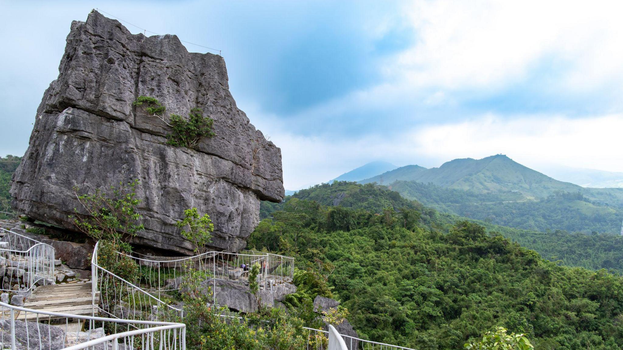 A large limestone boulder, with a footpath leading to it, against the backdrop of Masungi's lush rainforest. 