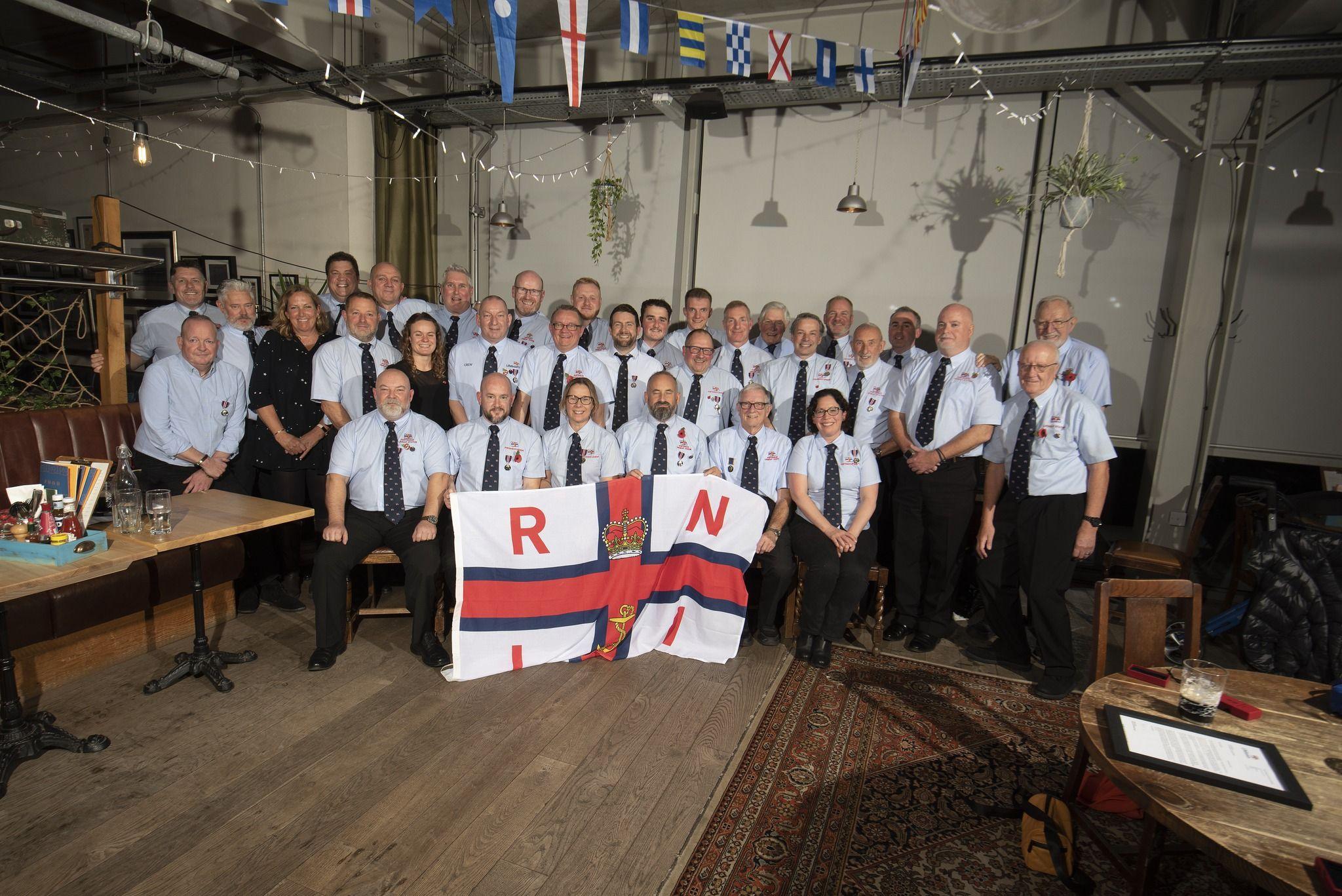 Volunteers in uniform at RNLI Portishead pose with a RNLI flag