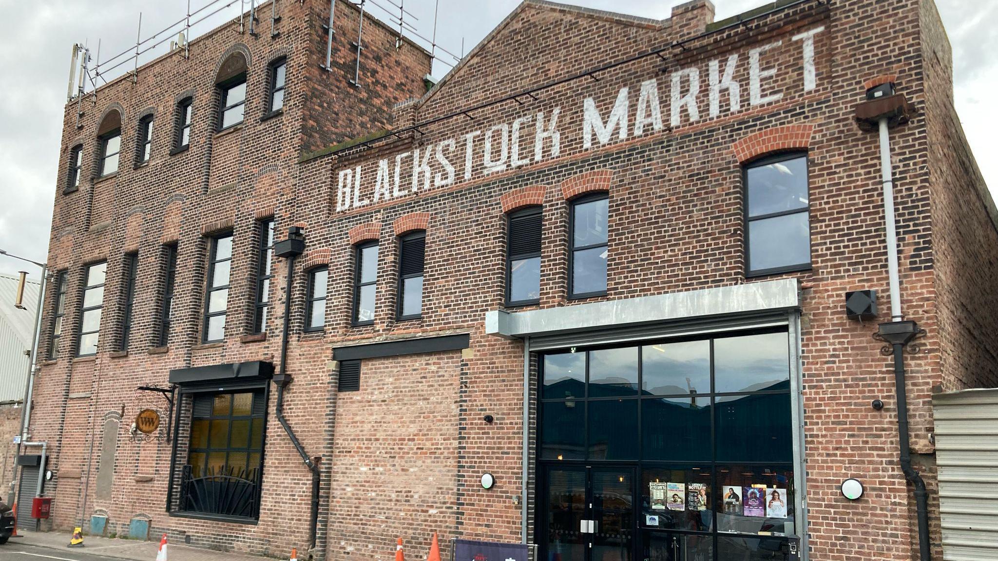 A brick dock warehouse building with a large black window and Blackstock Market painted in white