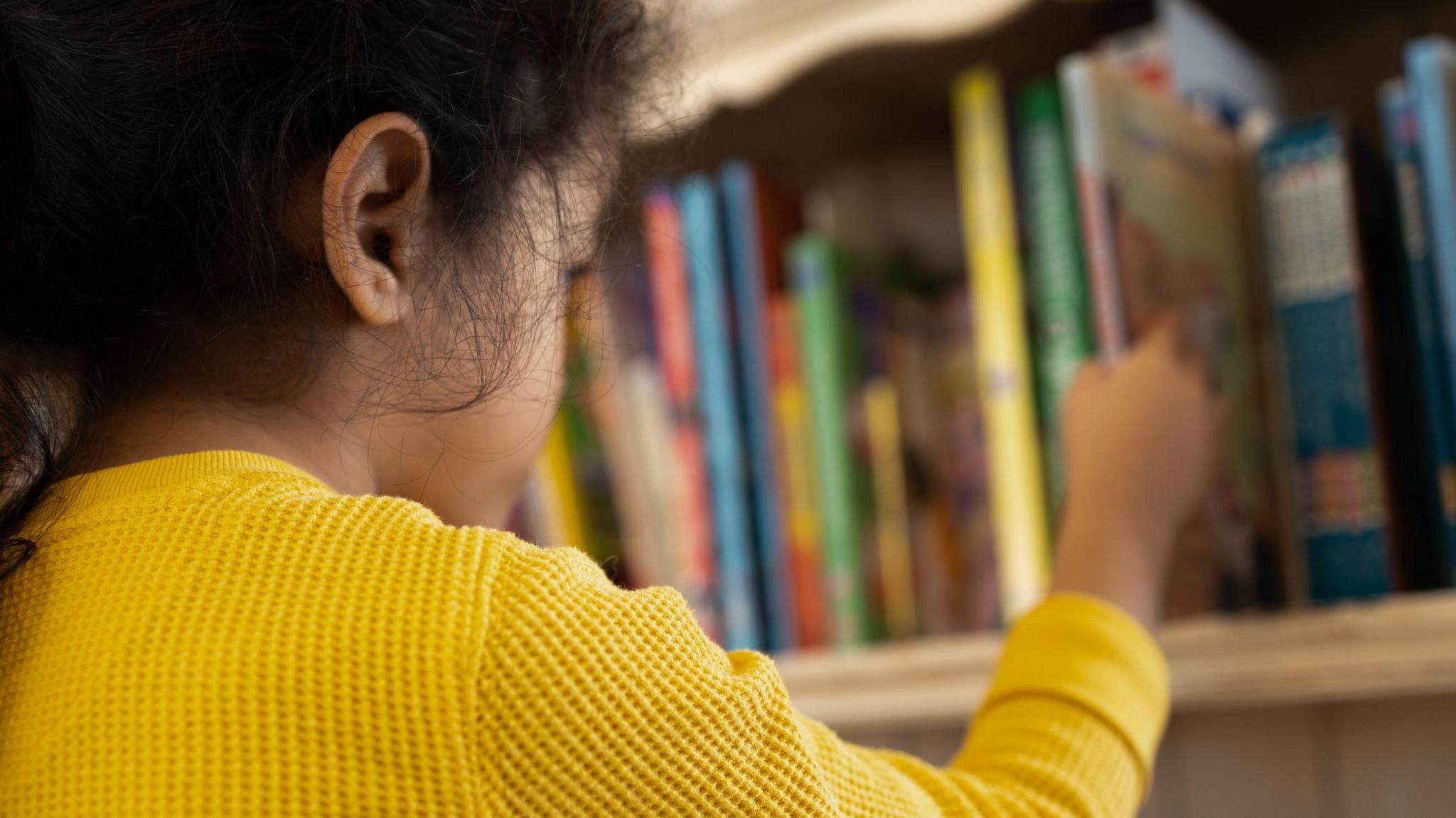 young girl reaching for a book off a shelf