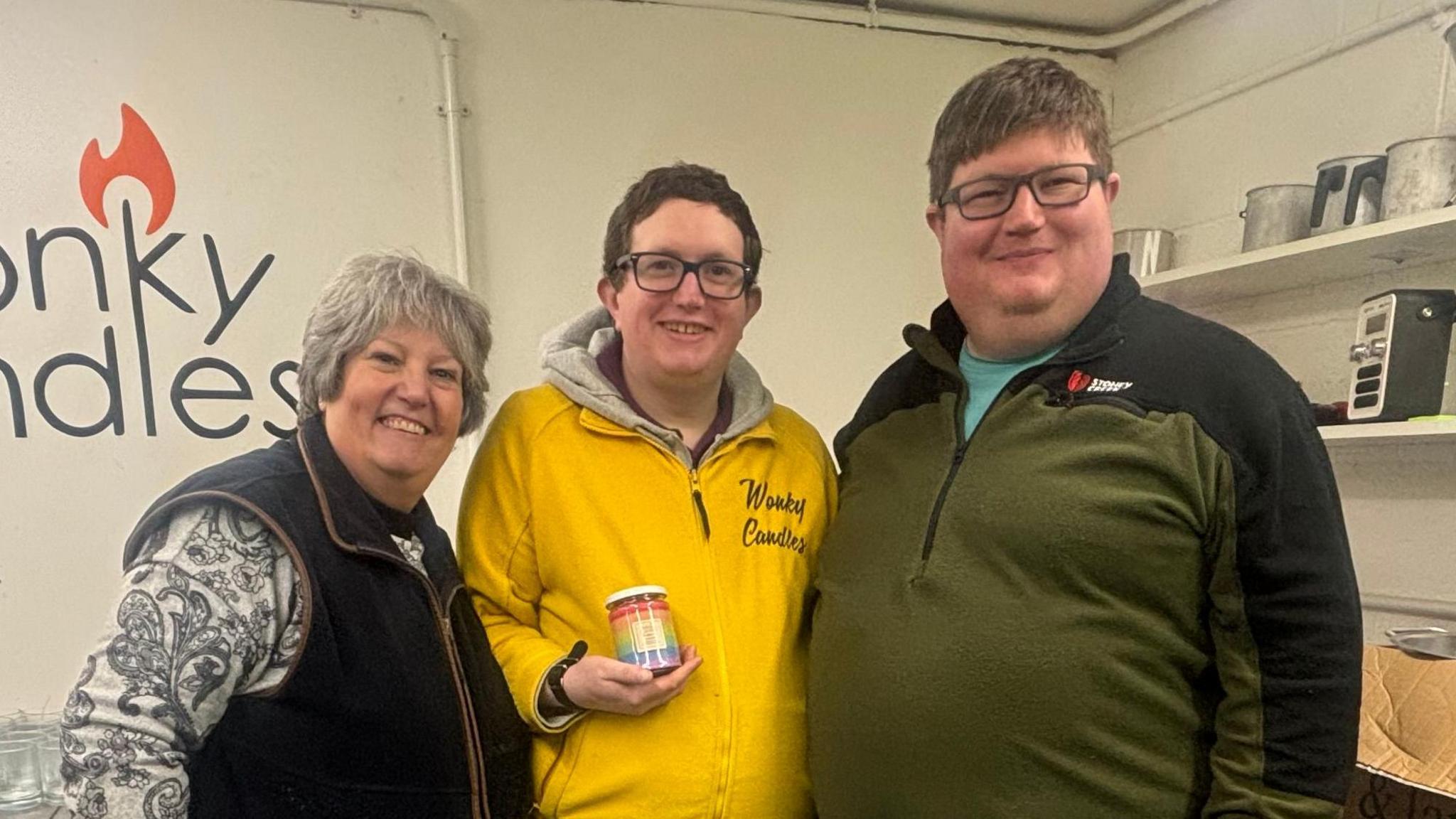 From left: Helen, PJ and Tom Seaman stood in the Wonky Candles workshop with metal shelves behind them and empty candle holders.