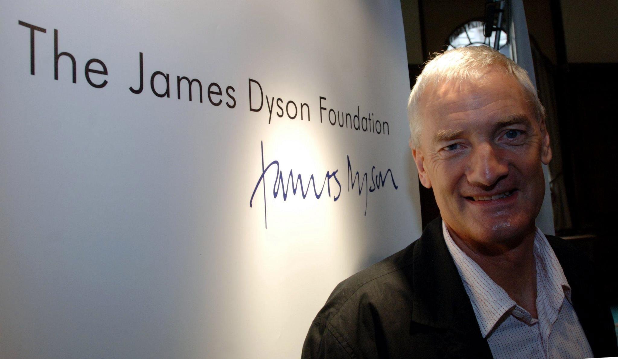 Man with grey hair, shirt and black jacket. He stands in front of a sign which says 'The James Dyson Foundation'