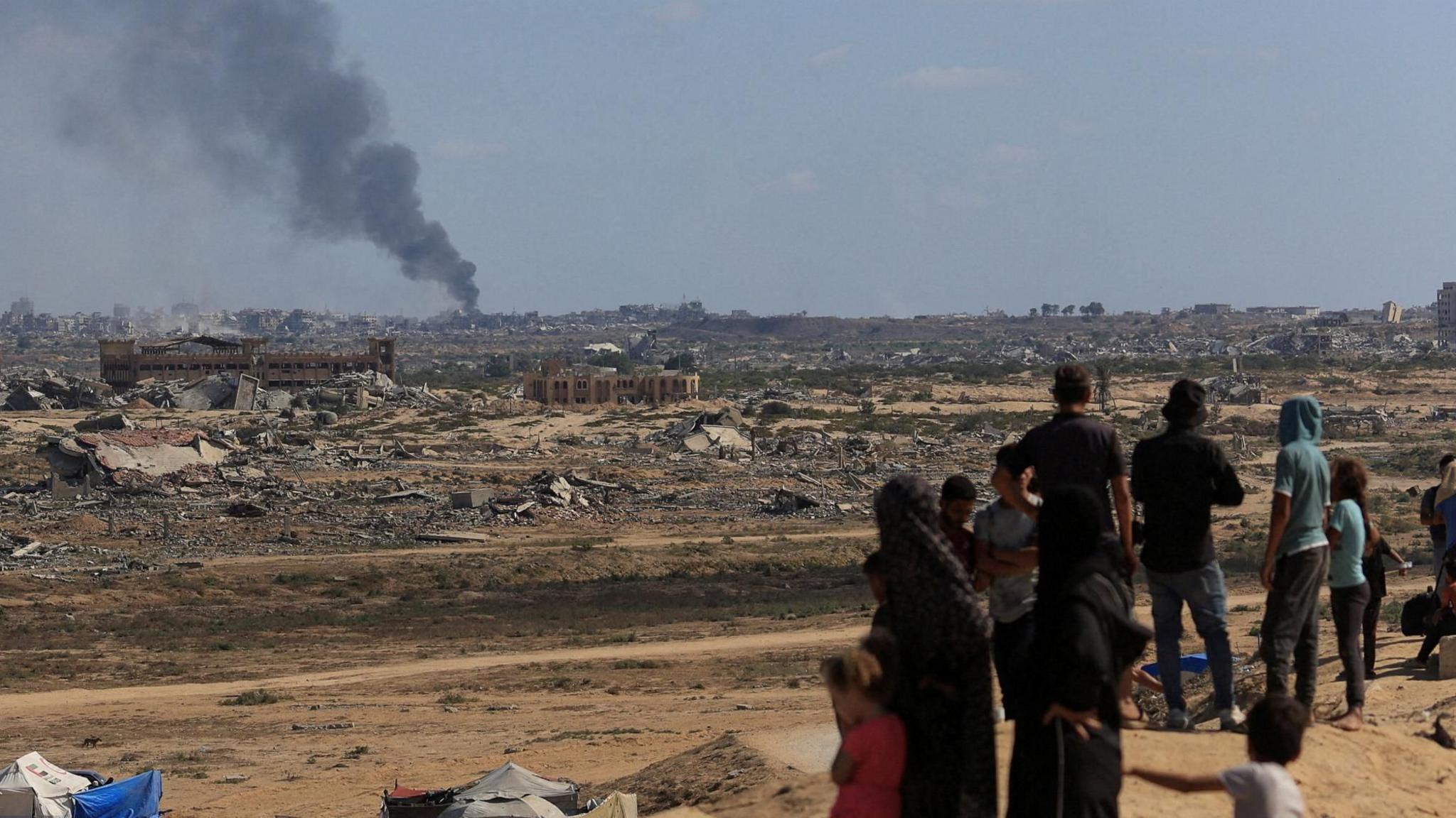 Palestinians watch as smoke rises during an Israeli military operation in Gaza City, as seen from the central Gaza Strip (2 October 2025)