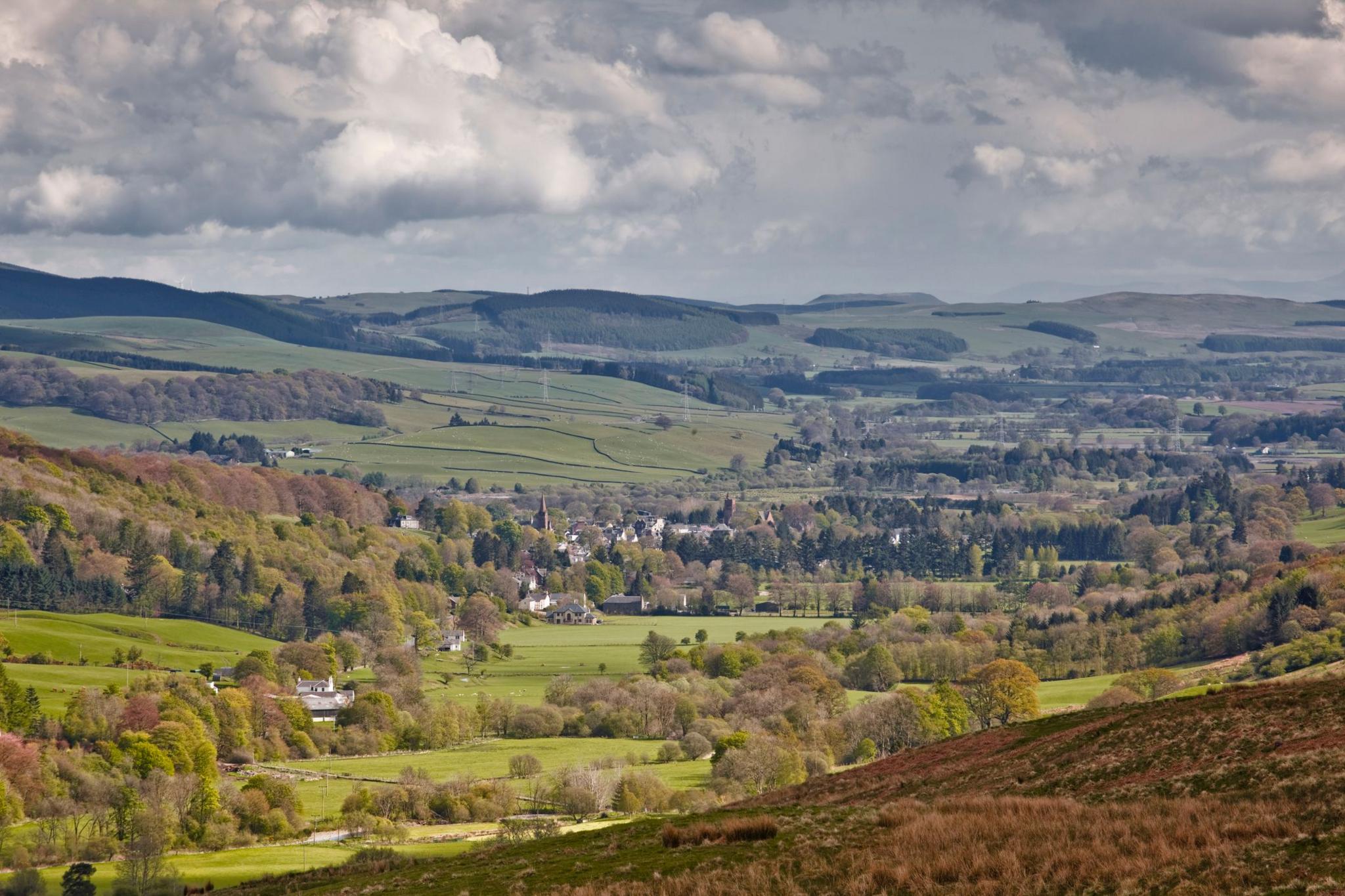 The town of Moffat in Dumfries and Galloway viewed from a distance. There is a large, tree-covered valley with houses in the middle of it.