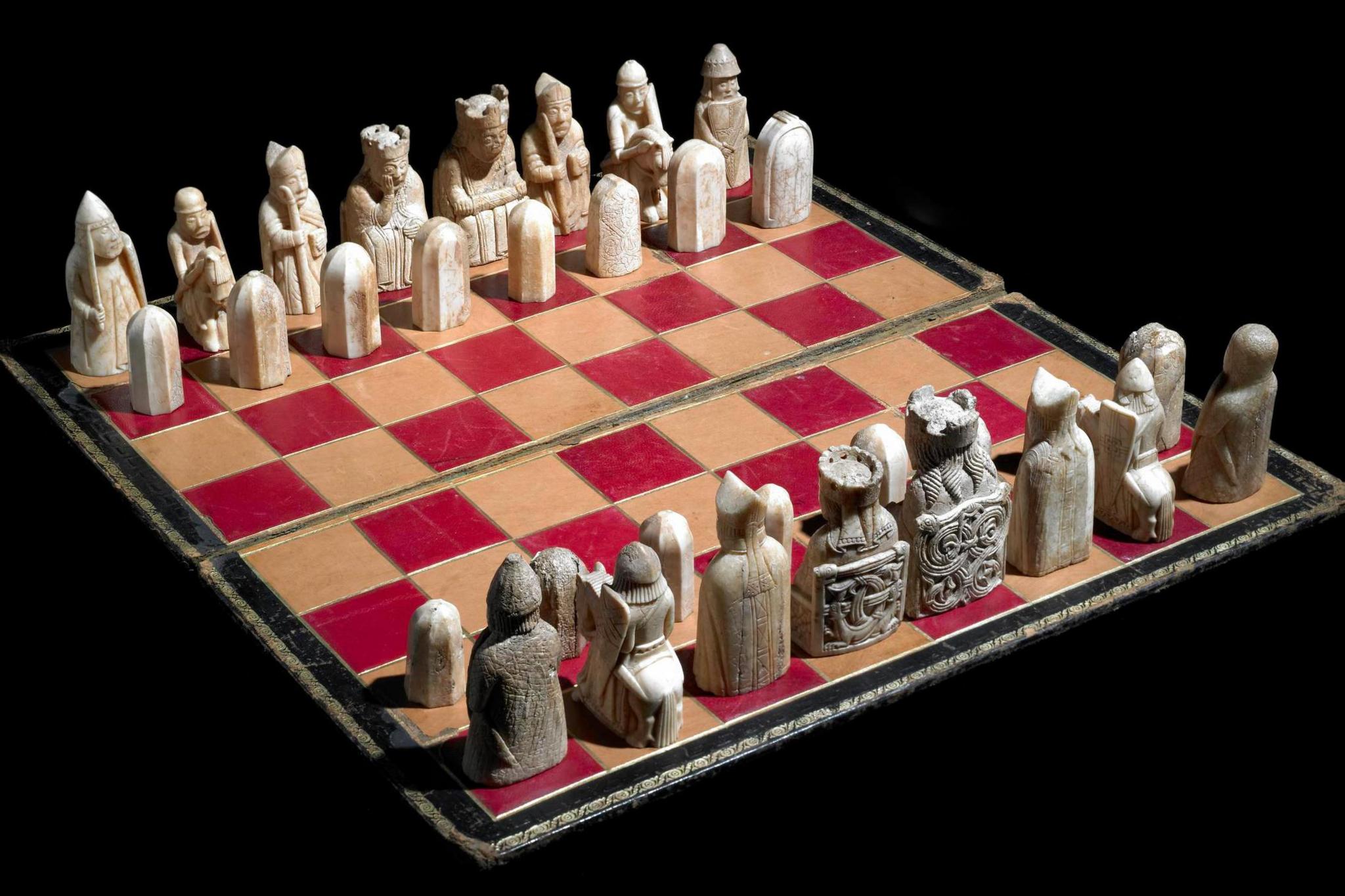 Images shows Lewis chess pieces, made of ivory from the 12th Century - on red & beige board