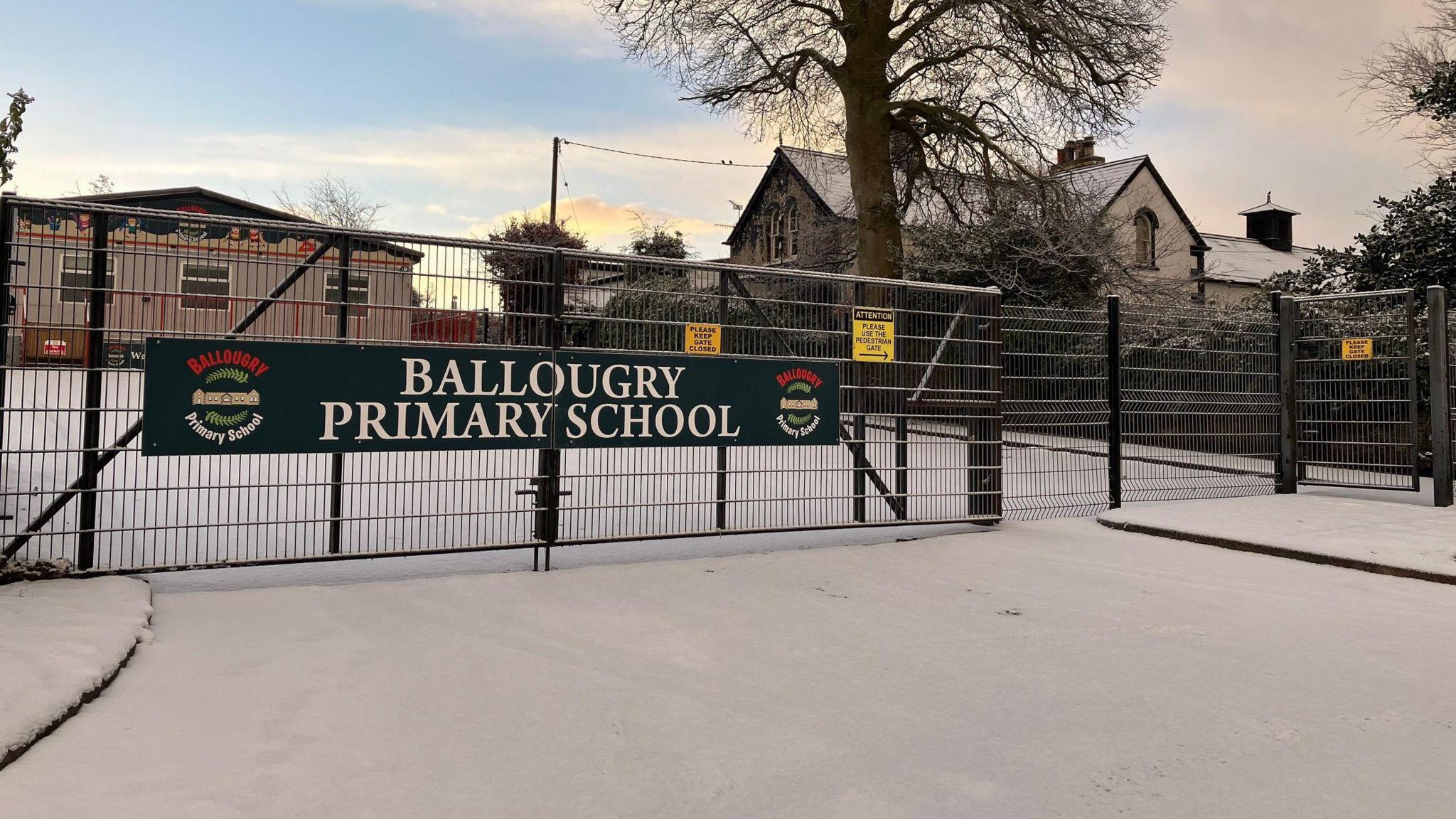 The front gate of a closed Ballougry primary school. Snow covers the entrance, and sits on the roofs of the two buildings that can be seen.