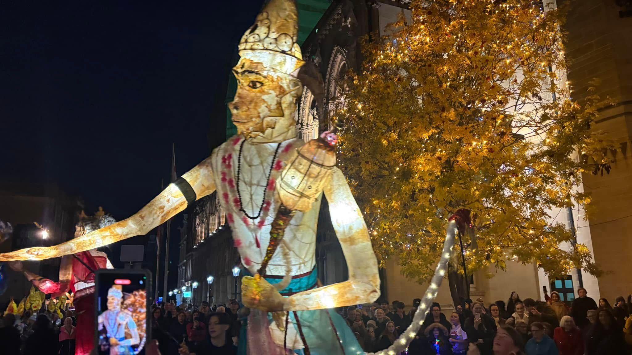 An illuminated large scale puppet, in the centre or Northampton, with crowds of people all around it. A tree has also been light up with lights.