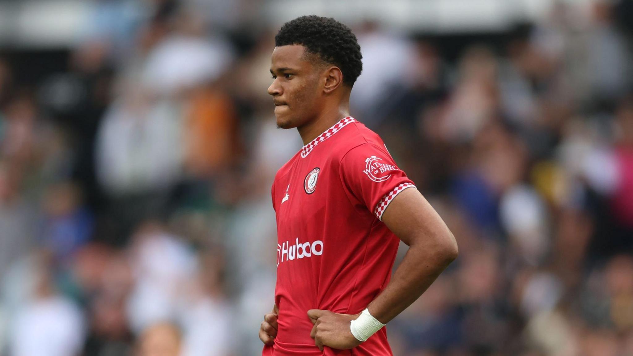 Fally Mayulu stands on the pitch with his hands on his hips