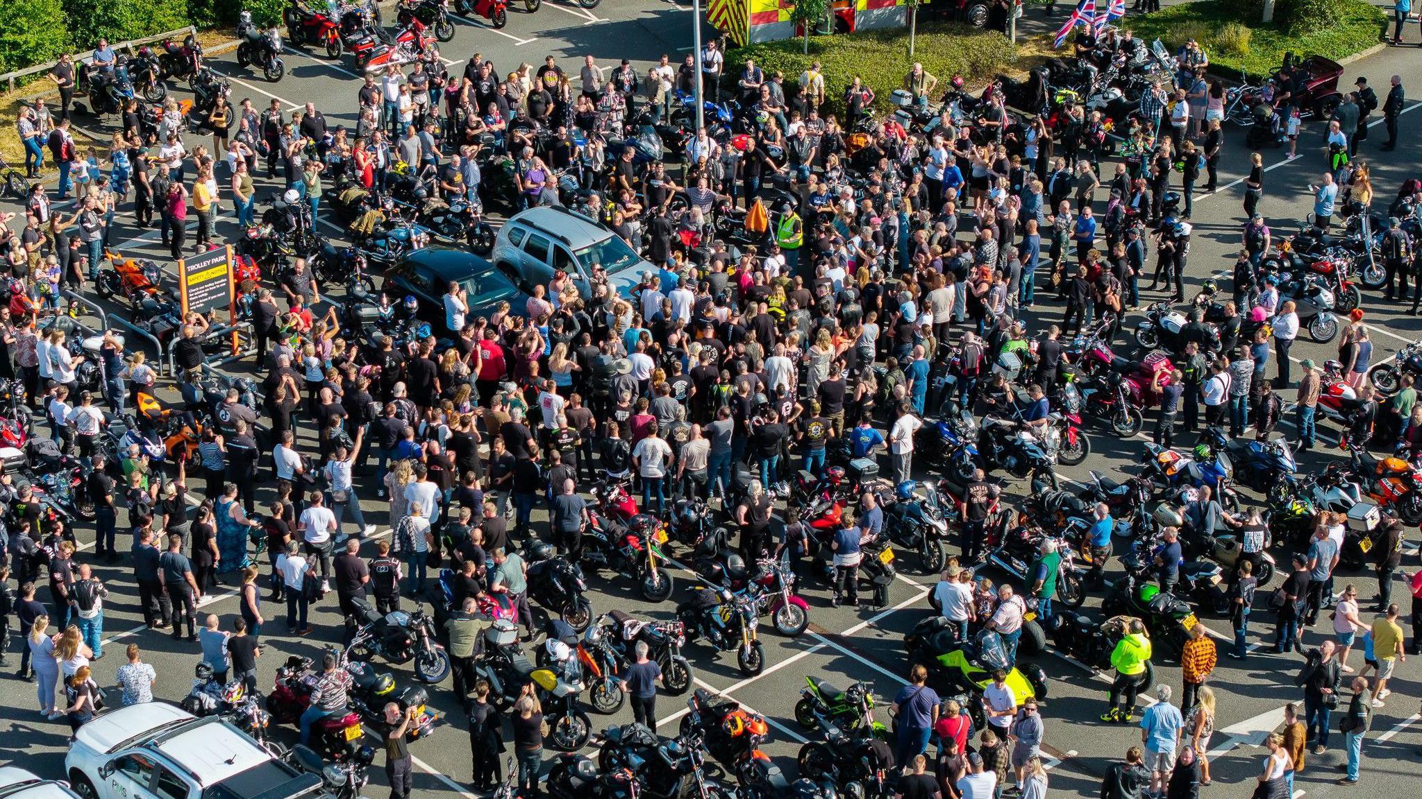 An aerial image showing hundreds of people gathered around Josh in a car park. The ground is barely visible as the crowd is densely packed together, and there are lots of motorbikes parked in spaces.