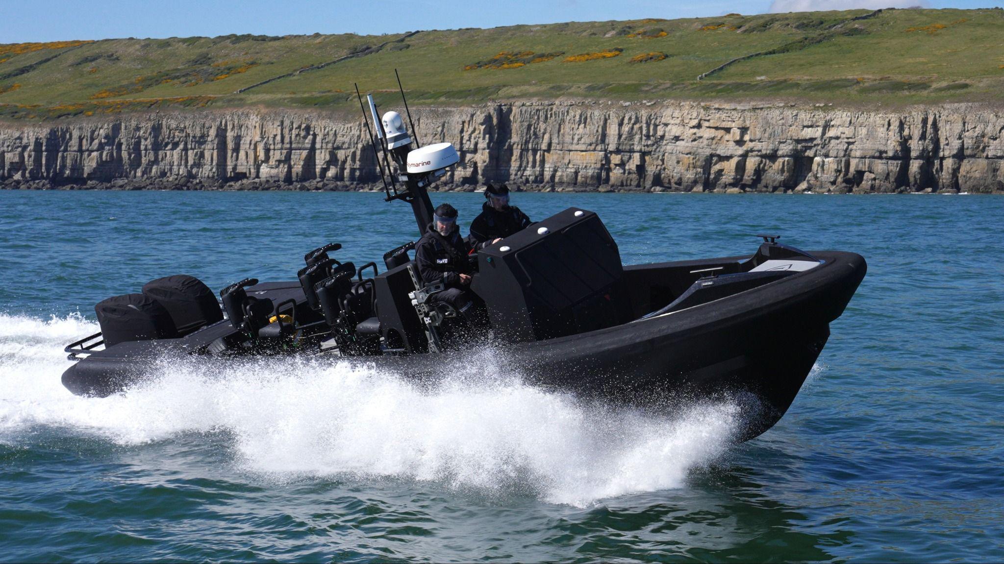 A black boat with two police officers travels quickly through the water near some cliff faces.