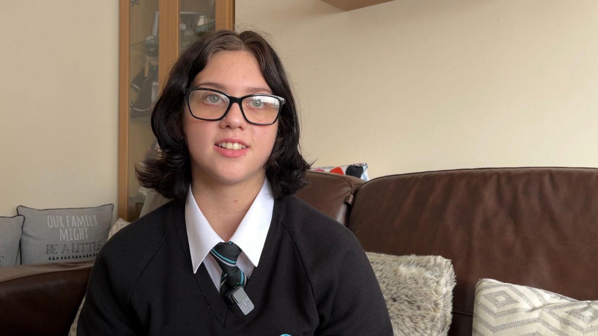 Lilly looking just past the camera, wearing glasses and her school uniform