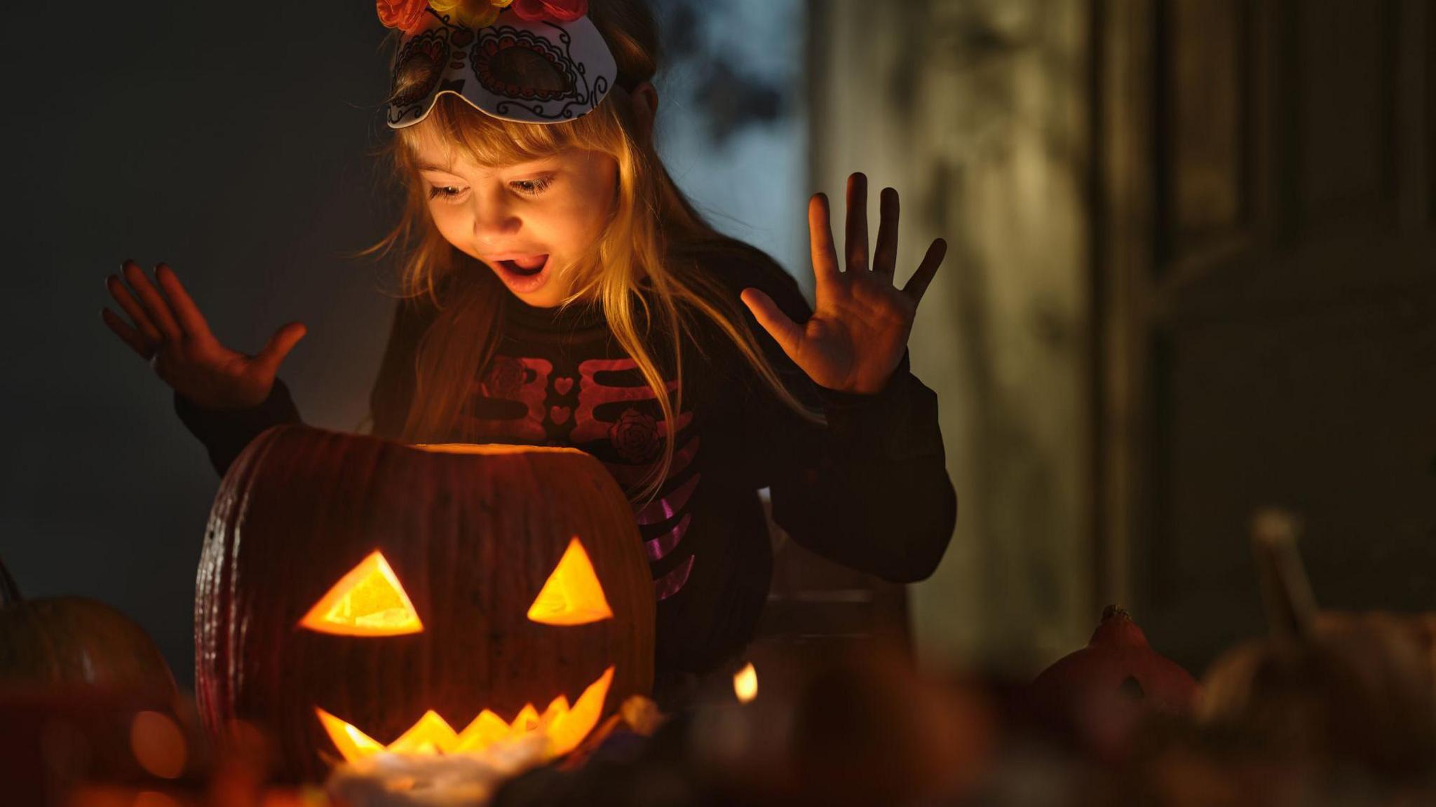 A young girl looks surprised whilst looking at her Halloween pumpkin