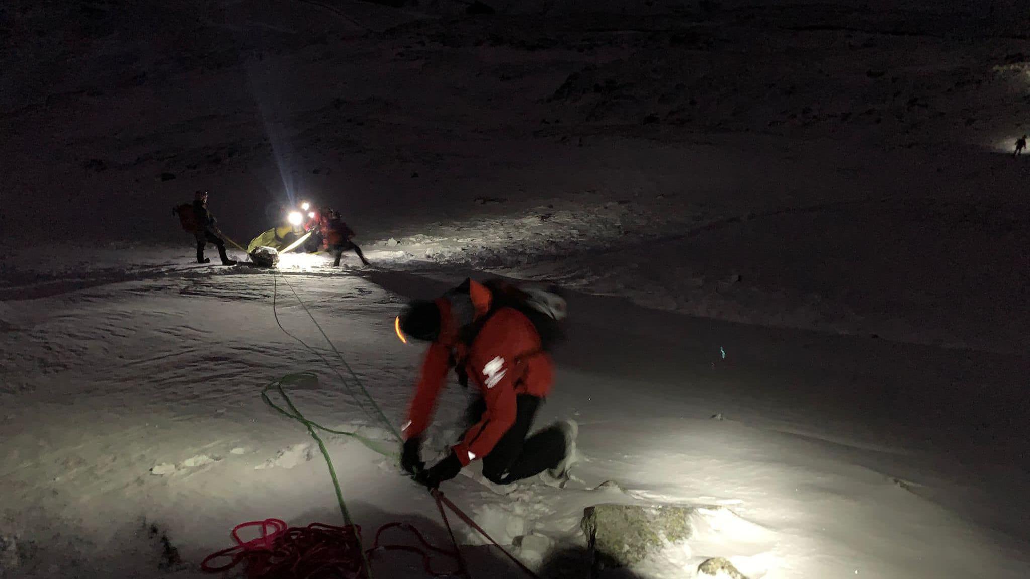 Man in orange jacket tying rope along snow using torch