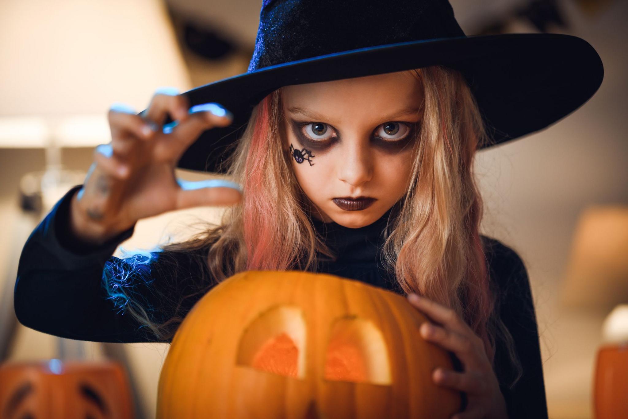 a girl dressed as a witch next to a carved pumpkin