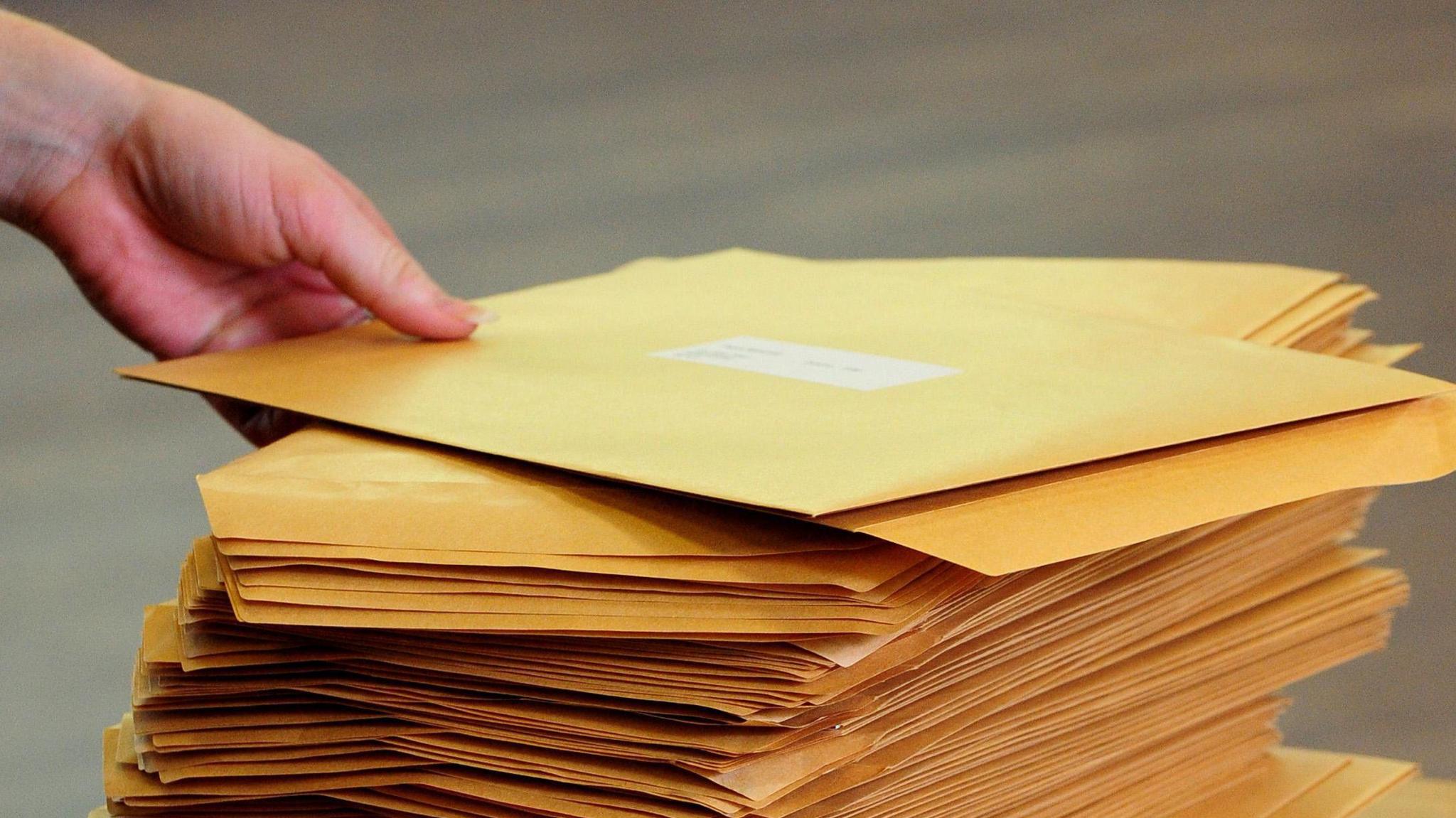 A set of envelopes on a table with a hand reaching in to pick one up