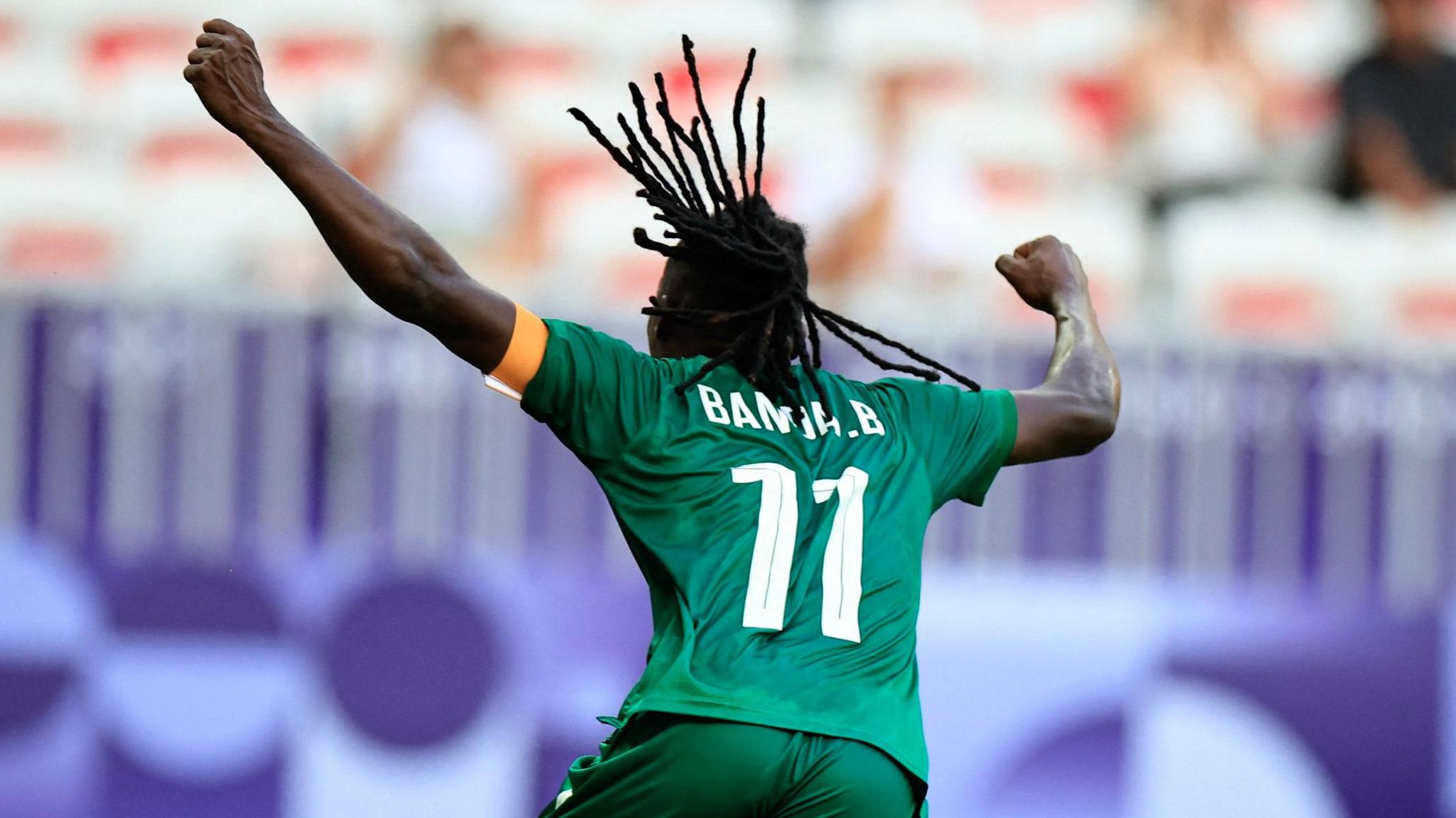 Barbra Banda, wearing a green shirt with her surname and the number 11 on the back, faces away from the camera as she punches the air in delight after scoring against Australia at the 2024 Olympic Games 