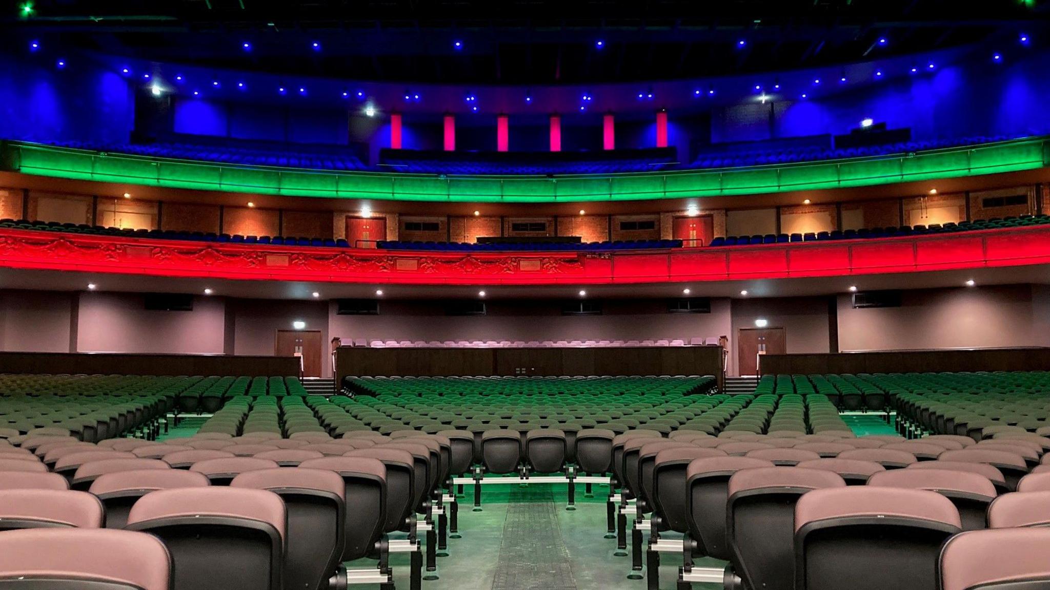 Rows of theatre-style seats with a multi-coloured dress circle in the background.