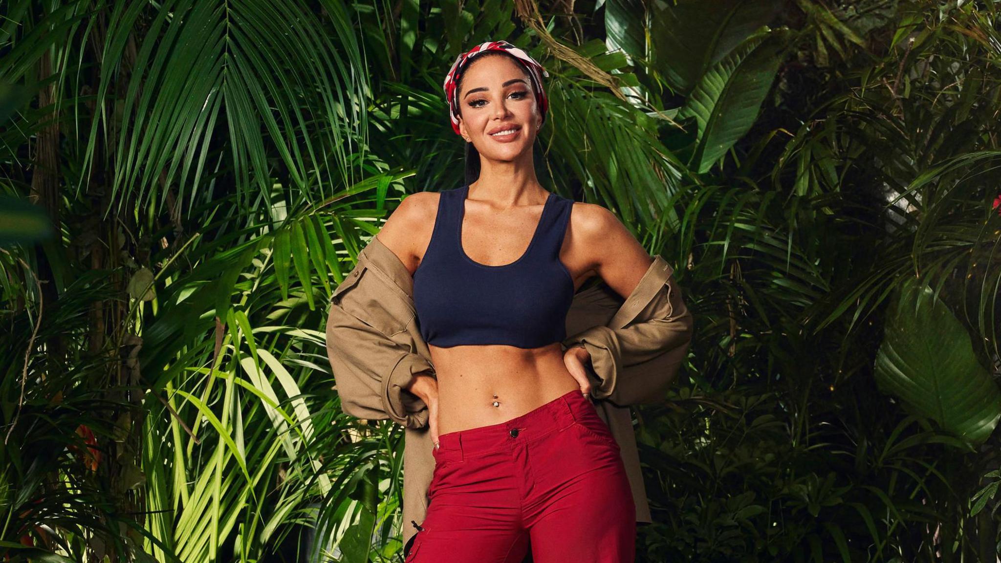 Tulisa wearing her jungle outfit, smiling and wearing a bandana, and surrounded by plants