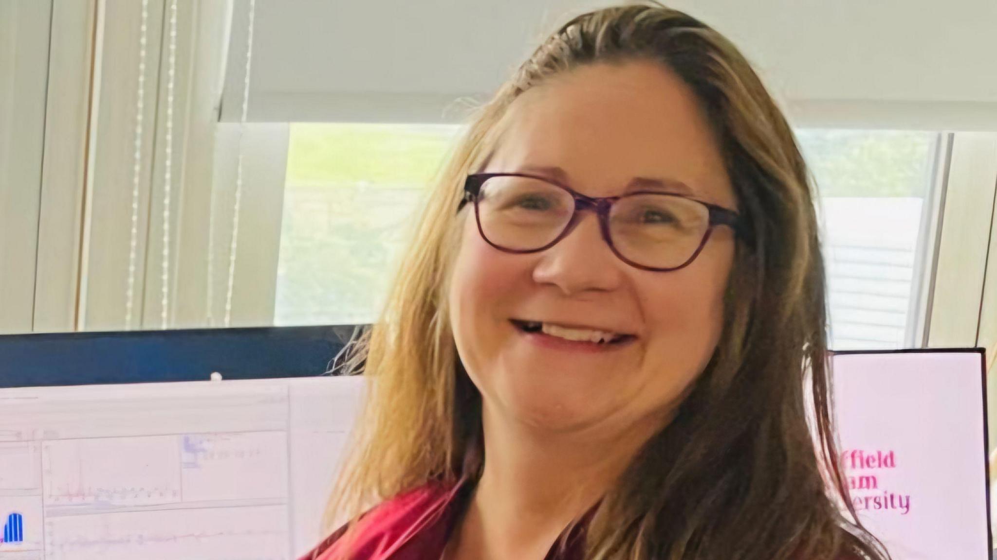 A woman with glasses and shoulder length straight hair smiles at the camera, Dr Sarah Haywood-Small