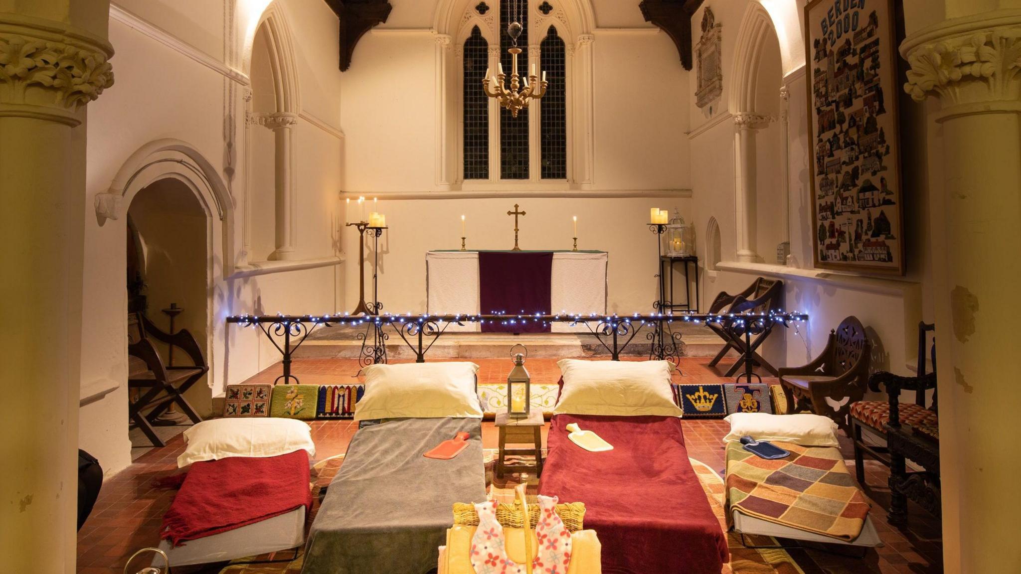 Four single beds set up in a church with an alter behind them.