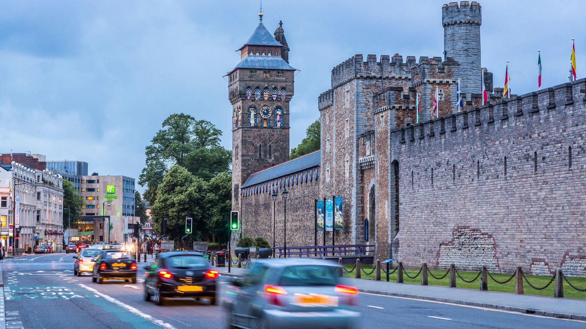 Wide image of the road which comes into Cardiff next to the Castle. Blurred cars can be seen driving through the city centre.