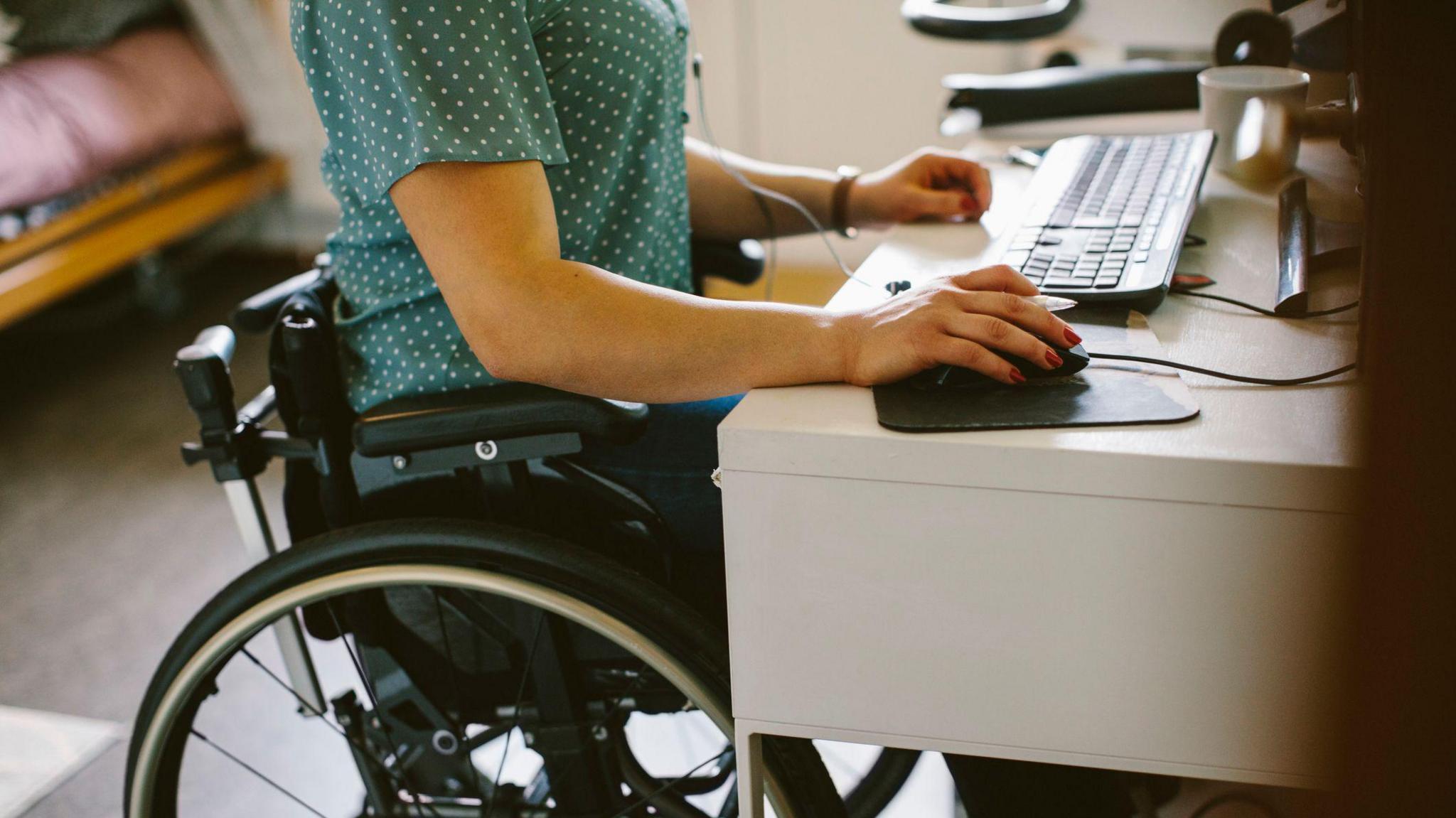 Young person in a wheelchair working at a computer on a desk from home