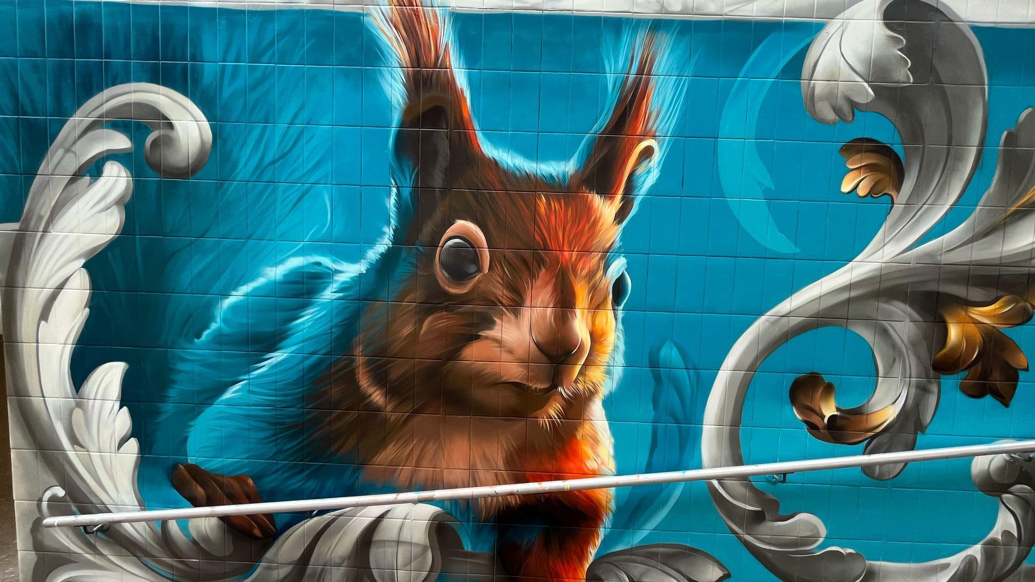 A blue mural with a red squirrel on the wall of the entrance to an underpass