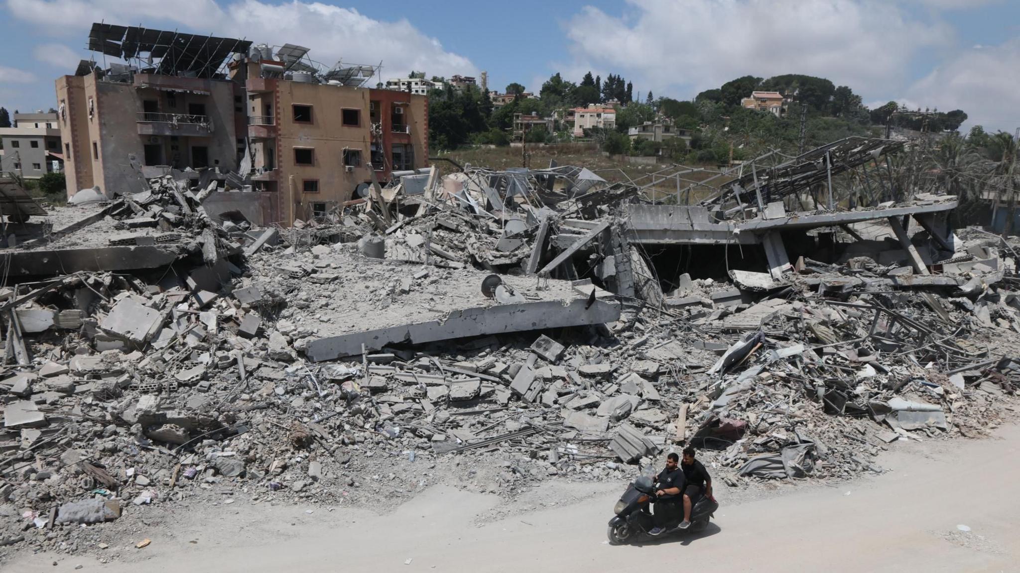 A man riding a motorcycle past destroyed buildings in the village of Mayfadoun, southern Lebanon (23 June 2026)