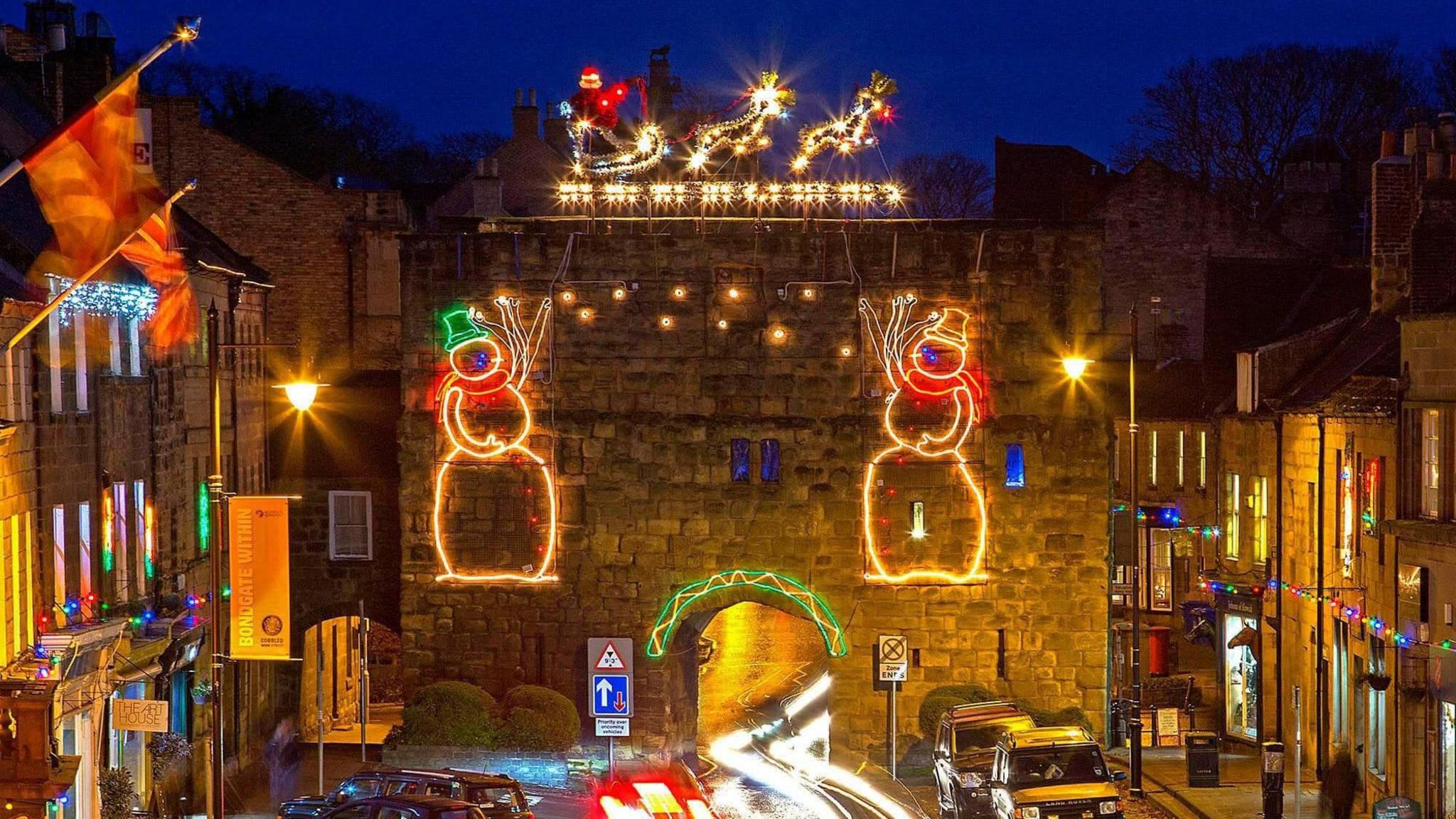 Bondgate Tower in Alnwick, which is a medieval structure consisting of a large gatehouse with a road running through a narrow arch in the middle, is covered with Christmas lights with Santa at the very top.