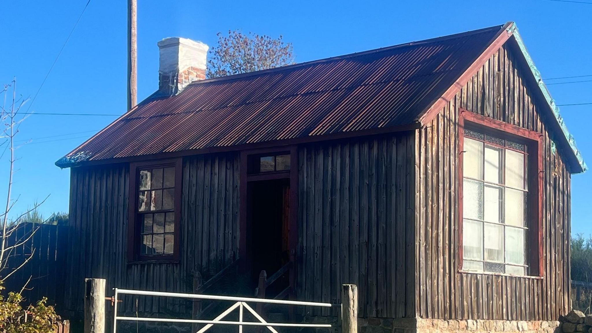Small building with wooden panels and a large window on one side. There's a smaller window and a door on the other side.